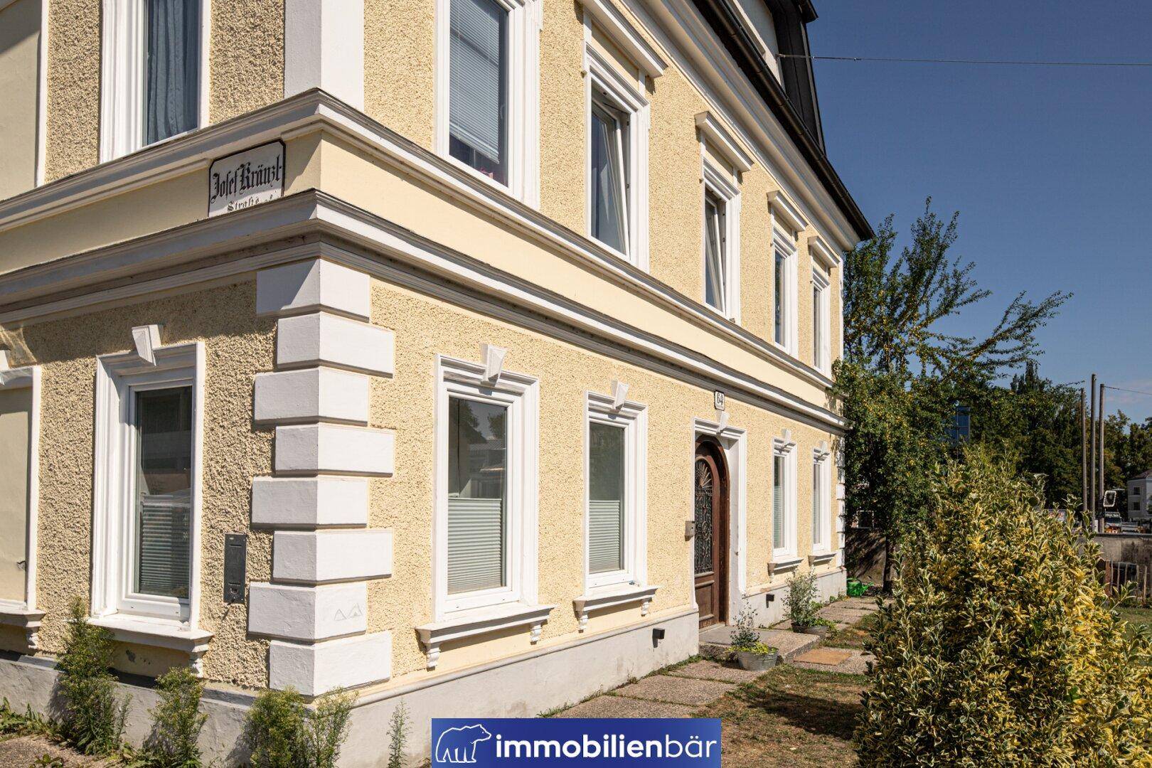 Nahaufnahme der gelben Fassade mit Stuckelementen und weißen Fenstern an der Gebäudeecke.