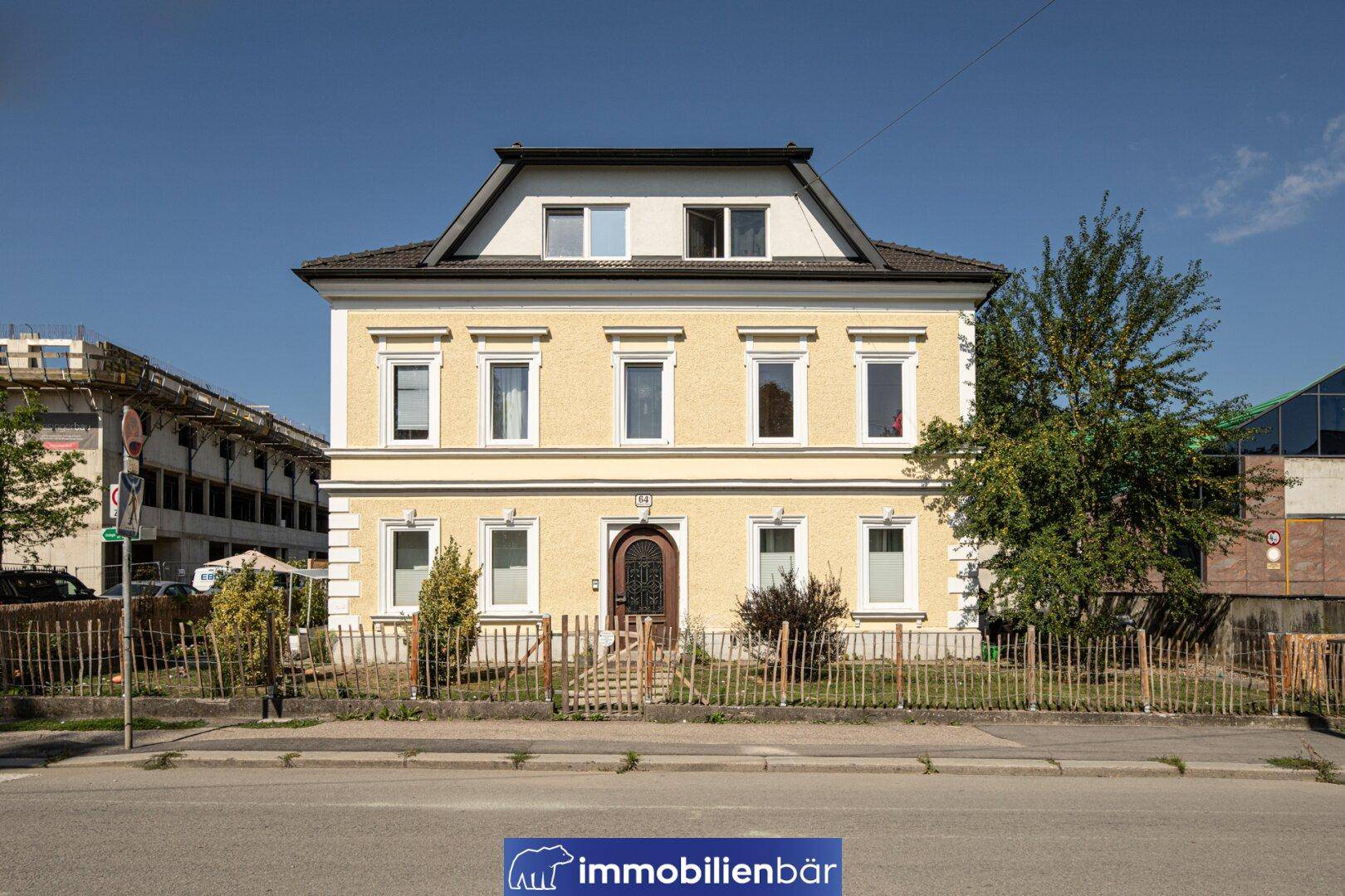 Frontansicht des charmanten gelben Gebäudes mit Holztür und kleinem Vorgarten an einer ruhigen Straße.
