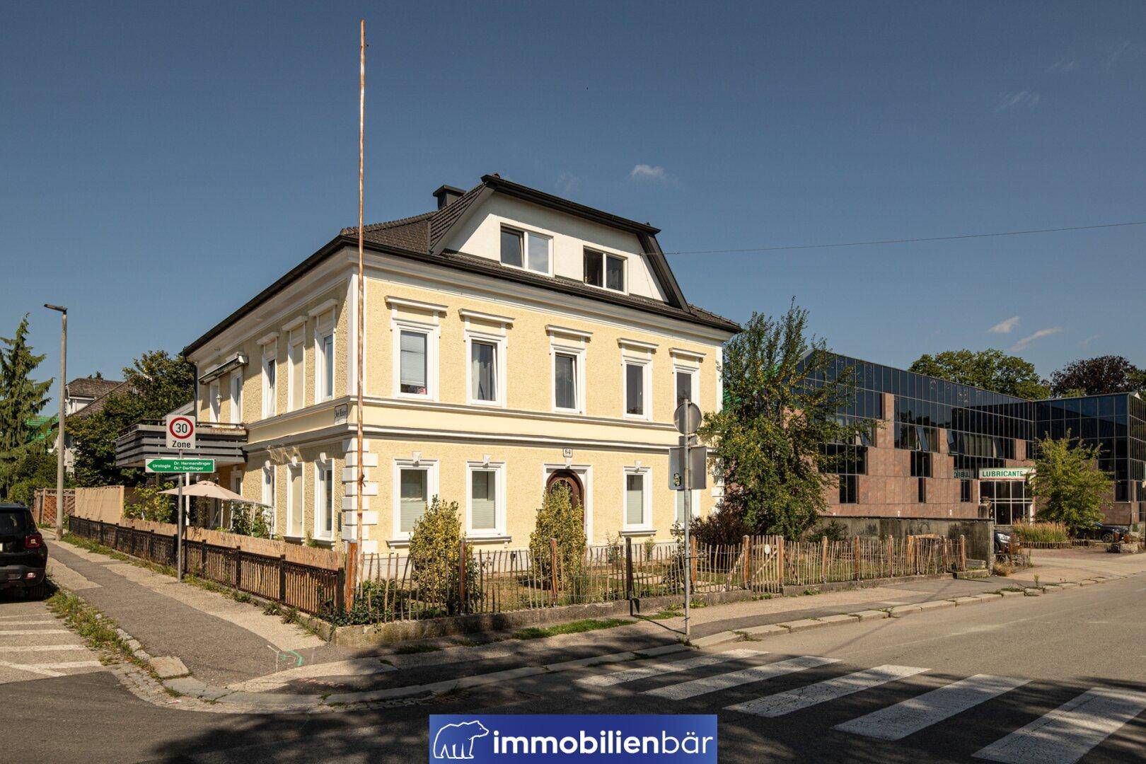 Das gelbe Gebäude an einer Straßenecke mit einem modernen Bürogebäude im Hintergrund unter blauem Himmel.