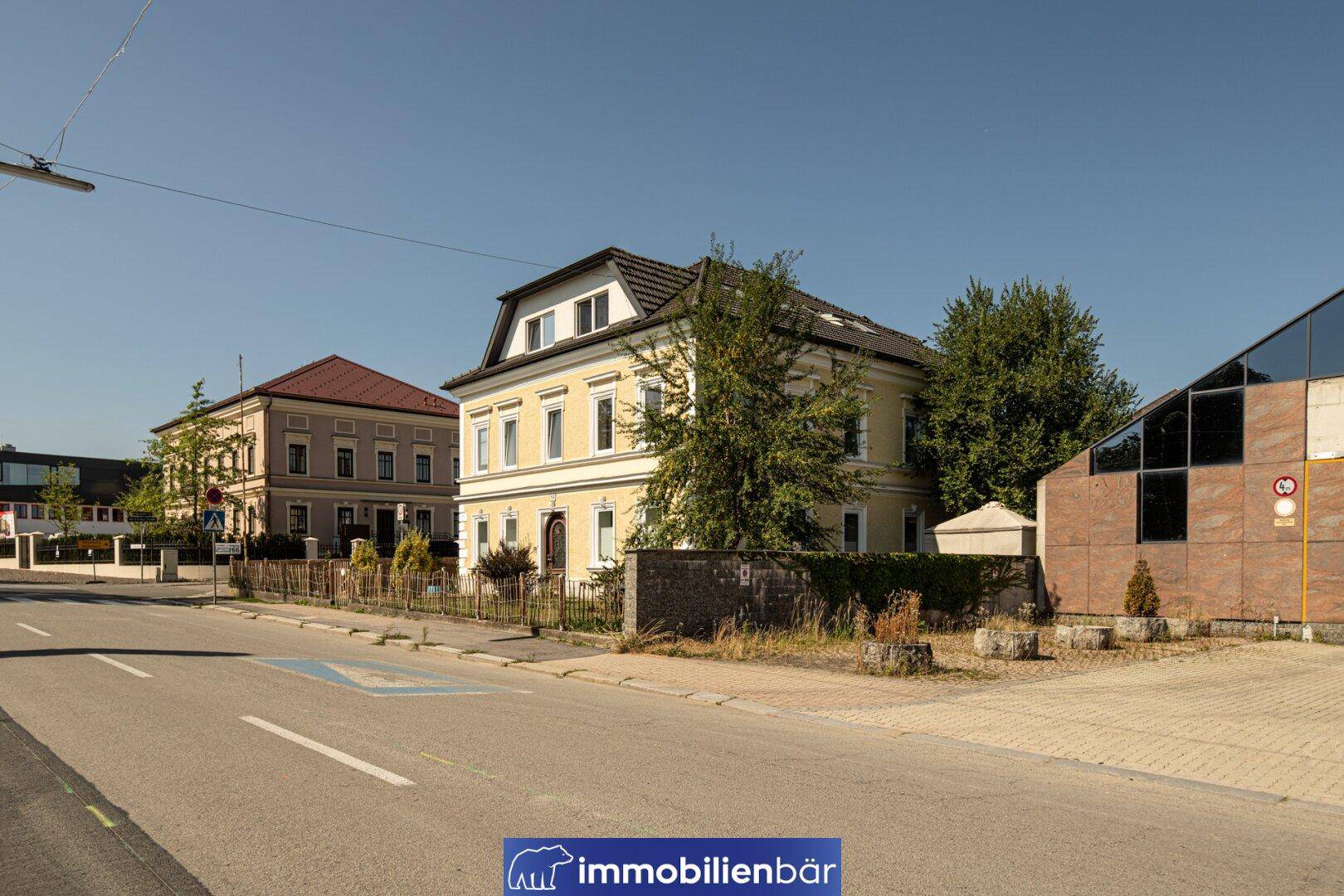 Ansicht des gelben Gebäudes in einer städtischen Umgebung mit angrenzenden Gebäuden und Straße.
