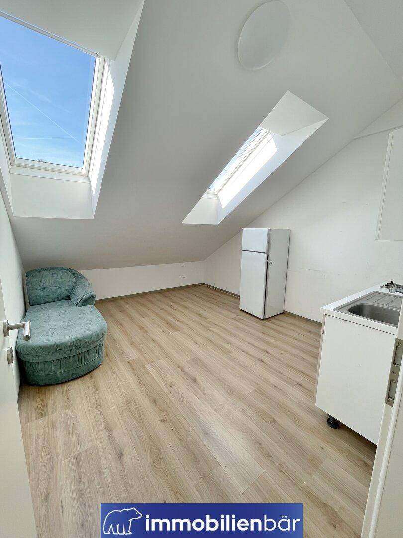 Dachgeschosszimmer mit Schrägdach, Dachfenstern, Kochnische und hellem Laminatboden.