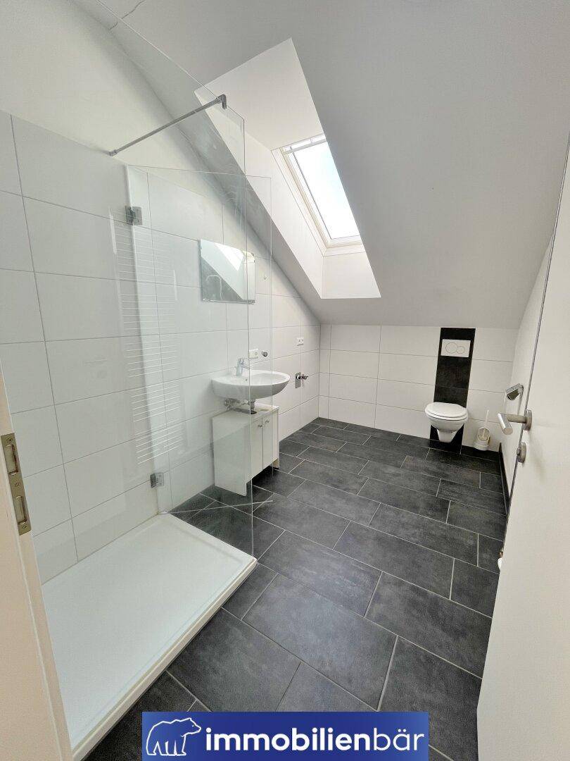 Modernes Badezimmer im Dachgeschoss mit begehbarer Dusche, dunklen Fliesen und Dachfenster.