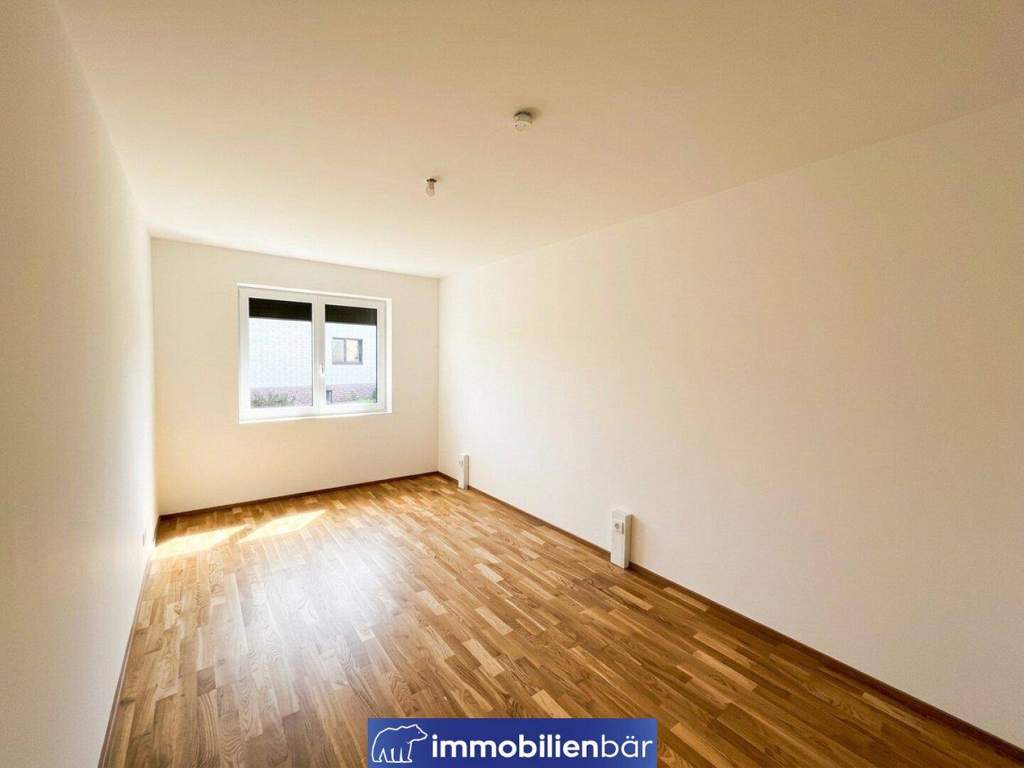 Unmöbliertes Schlafzimmer mit hellem Parkettboden, weißen Wänden und Fenster.