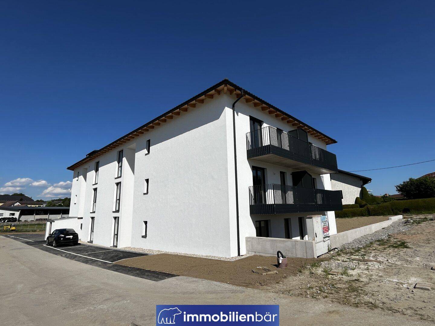 Moderne Wohnanlage mit weißer Fassade und ausreichend Parkmöglichkeiten im Freien.