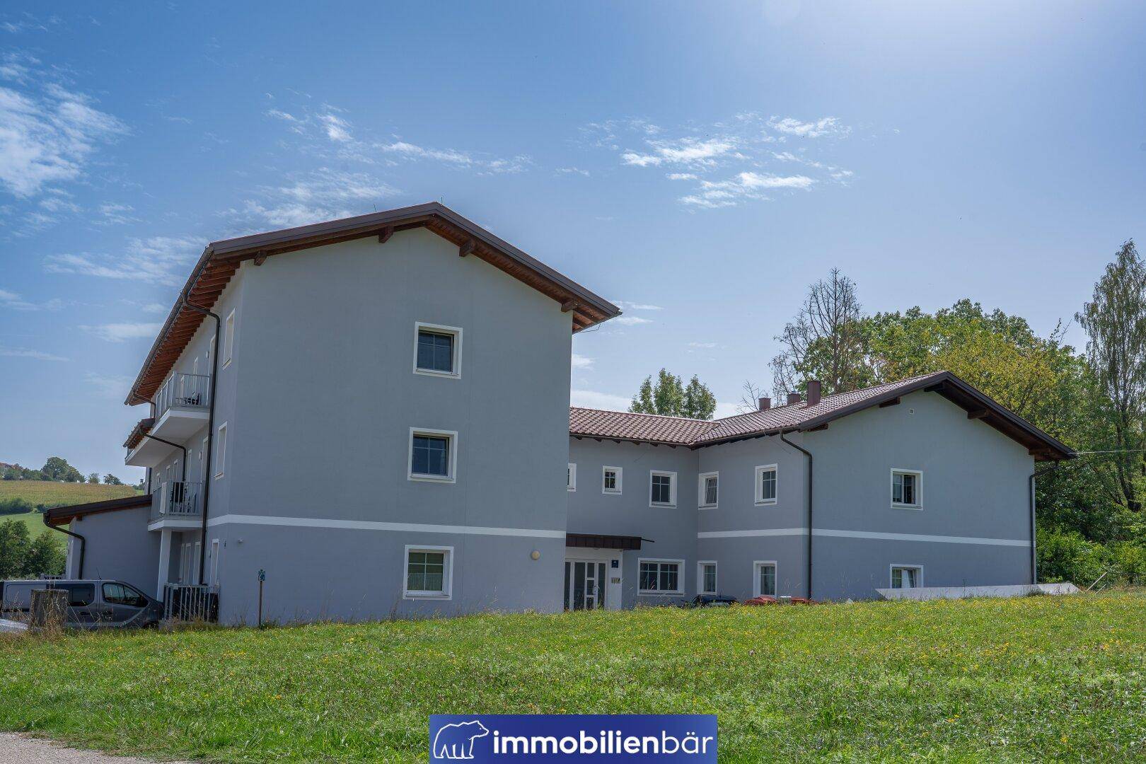 Rückansicht eines modernen Wohngebäudes mit gepflegter Grünfläche und weitem Blick in die Landschaft.