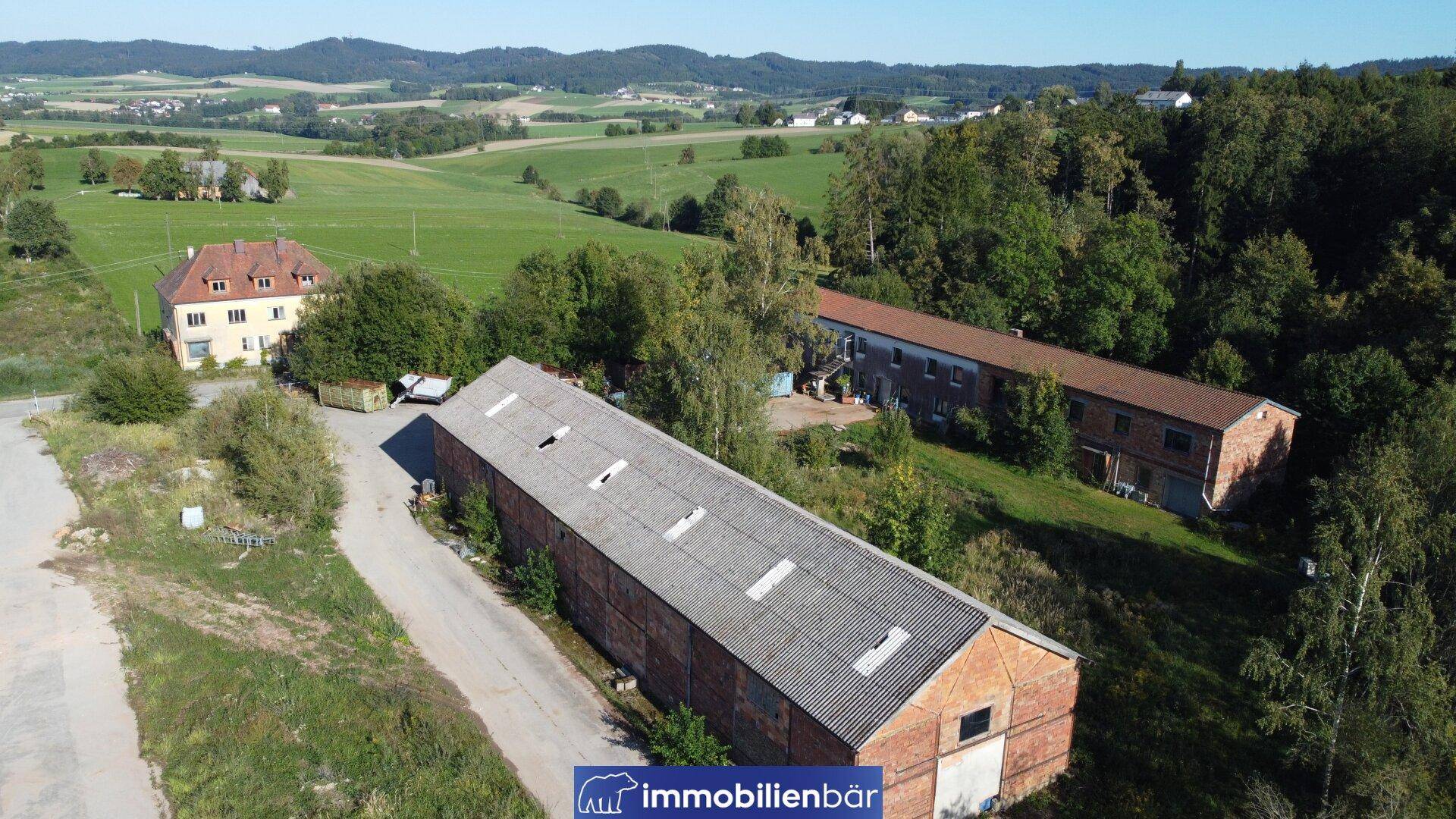 Luftaufnahme eines weitläufigen Anwesens mit mehreren Gebäuden, umgeben von Feldern und Wäldern.