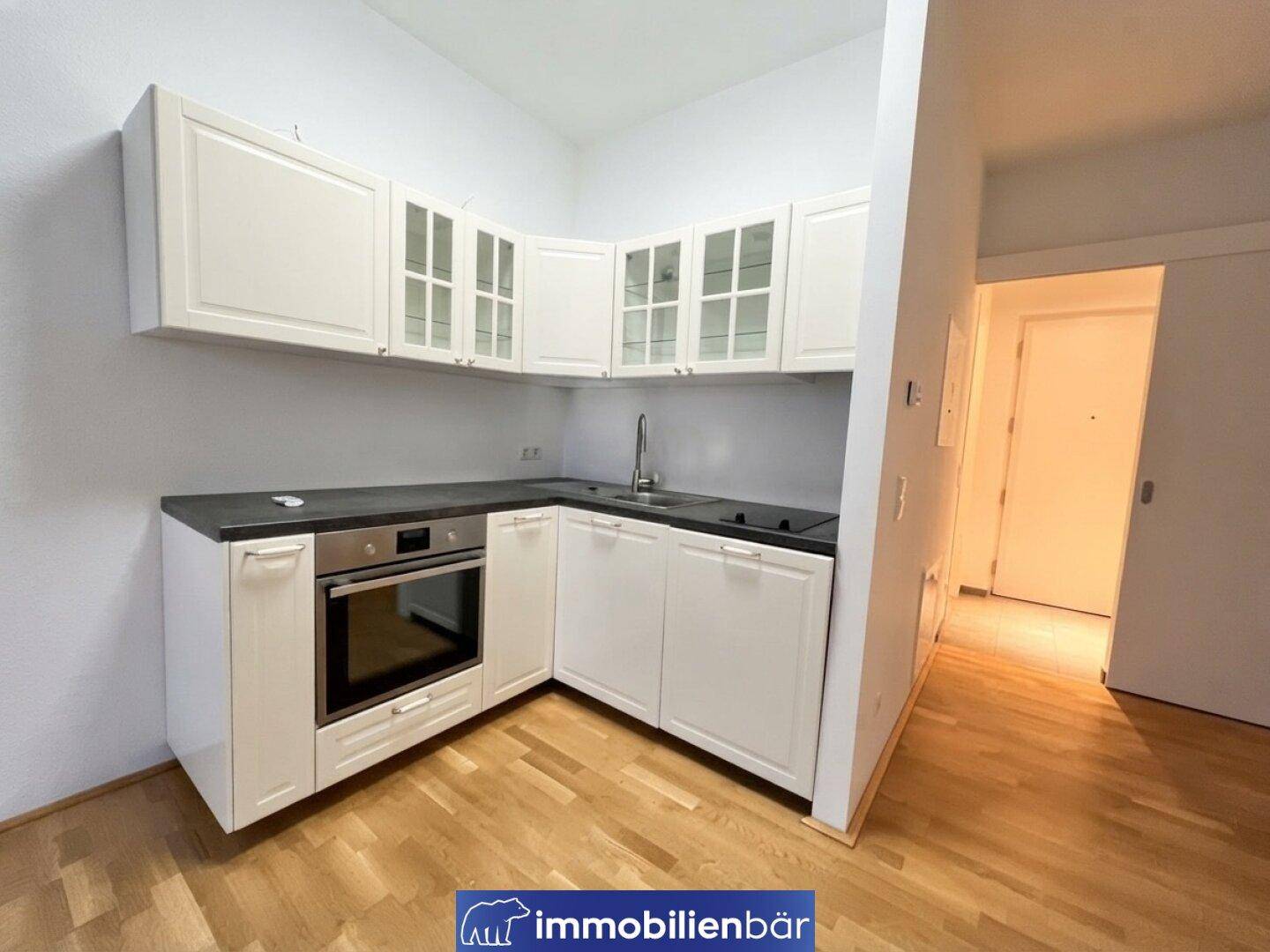 Moderne Küchenzeile mit weißen Schränken, dunkler Arbeitsplatte und integriertem Backofen.