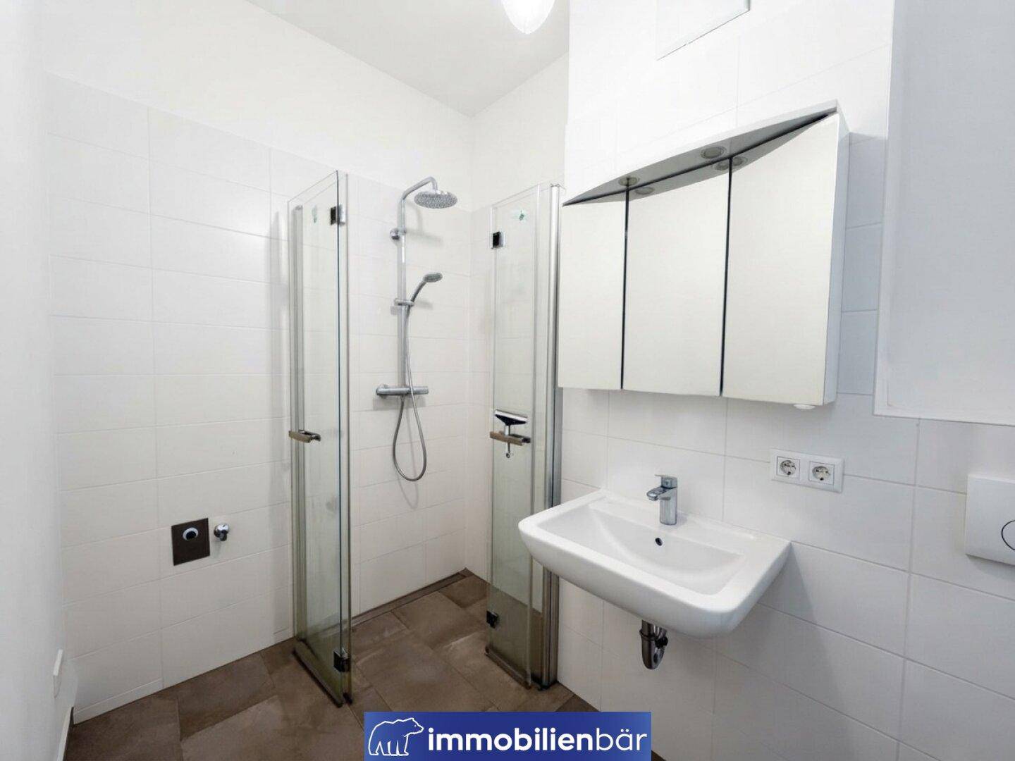 Funktionales Badezimmer mit weißen Wandfliesen, dunklem Fliesenboden und Duschbereich.