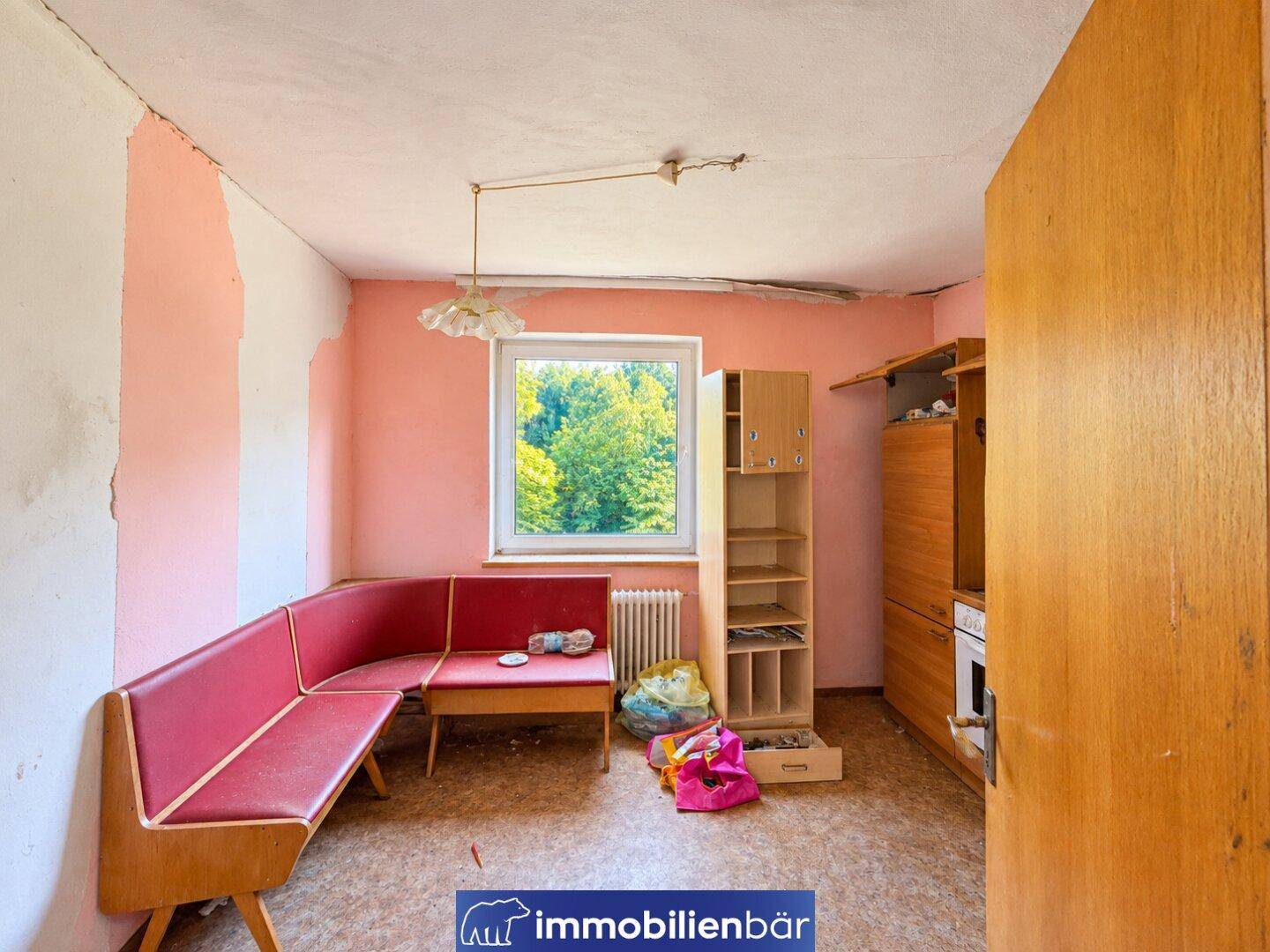 Zimmer in schlechtem Zustand mit Eckbank, alten Möbeln und abblätternder Tapete.