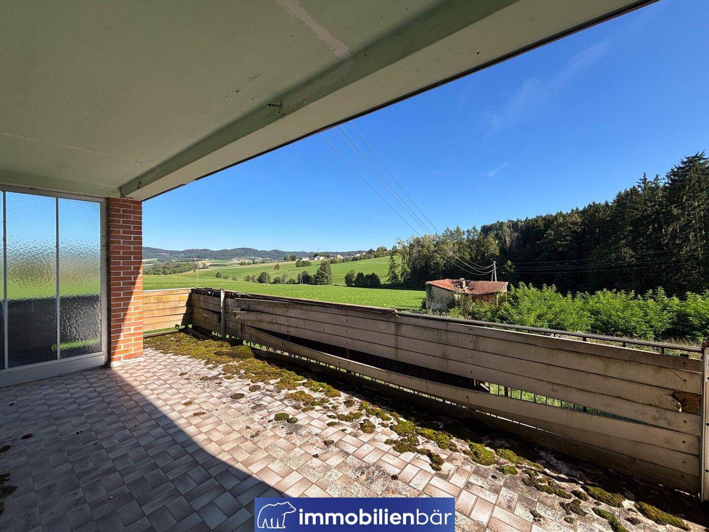 Ein überdachter Balkon mit Fliesenboden und einem weiten Blick über die ländliche Umgebung.