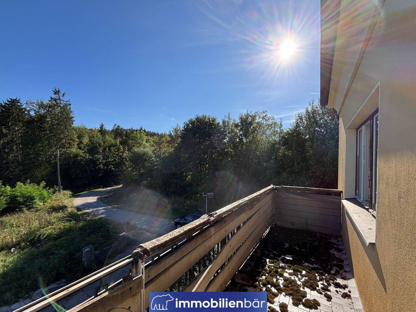 Ein sonniger Balkon mit Blick auf Bäume und eine Straße, der Renovierungsbedarf zeigt.