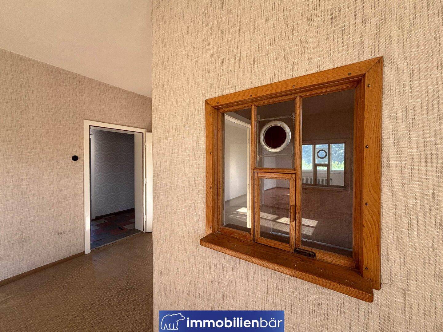 Nahaufnahme eines Holzfensters in einem Flur, das einen Blick in einen weiteren Raum ermöglicht.