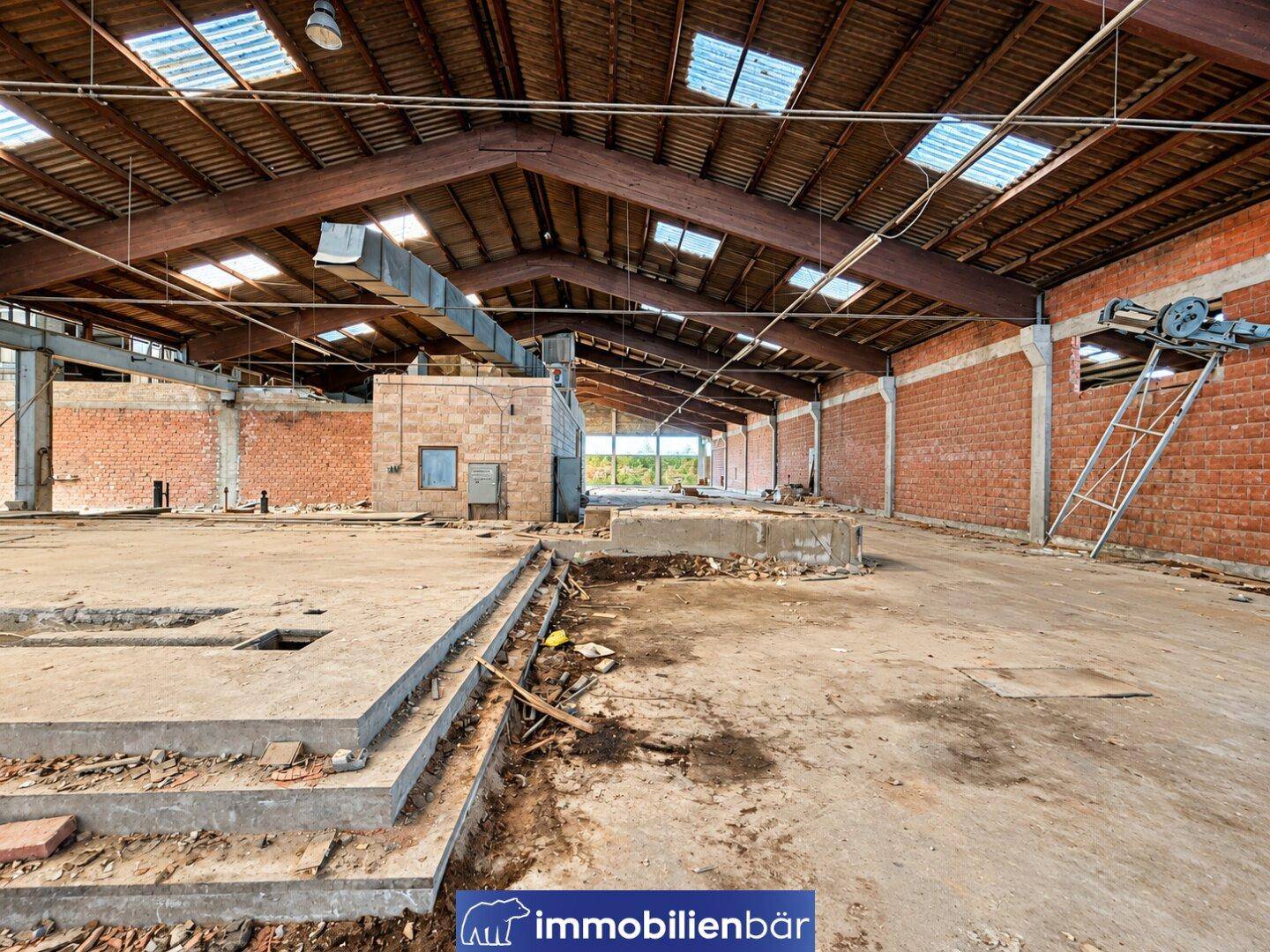 Große Industriehalle mit freiliegenden Holzbalken, Oberlichtern und Ziegelwänden, die auf eine frühere Nutzung hinweisen.