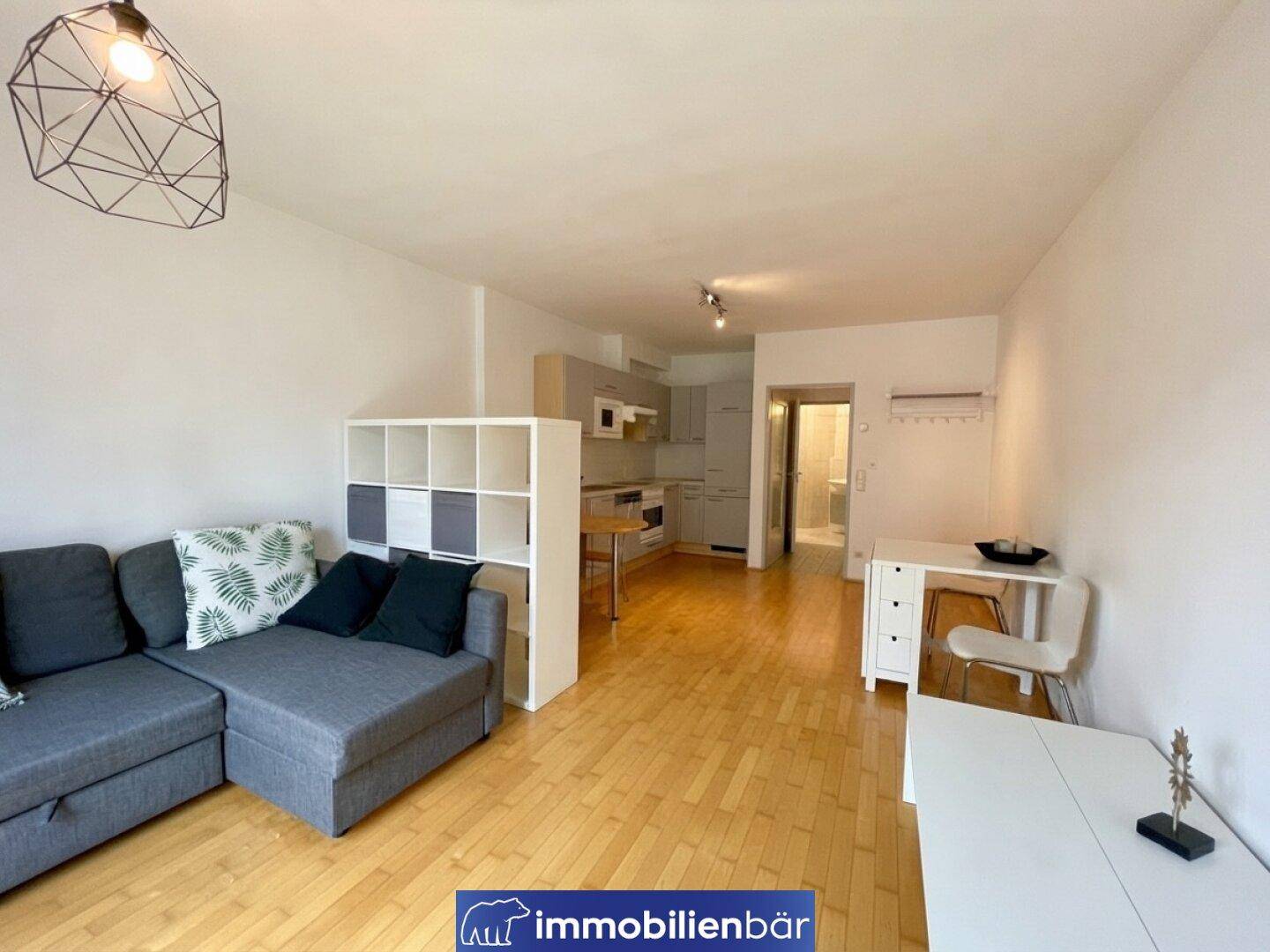 Gemütlicher Wohnbereich mit Sofa, Regal und offenem Übergang zur Küche und zum Badezimmer.