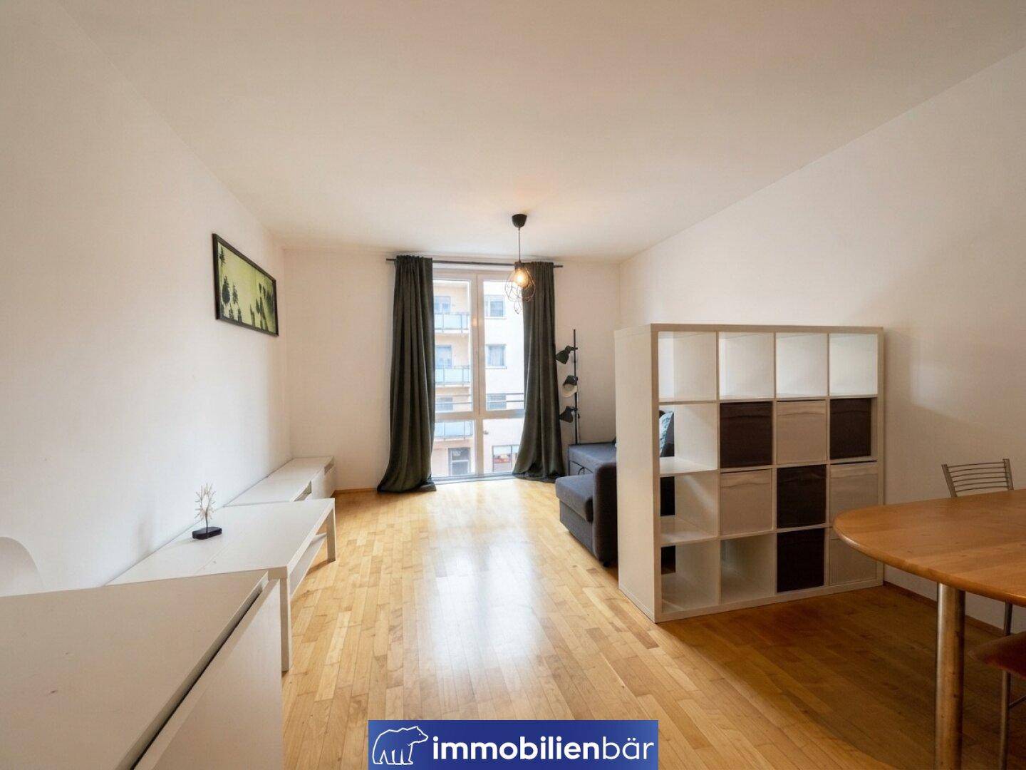 Wohnzimmer mit Holzboden, Esstisch und einem großen Fenster, das viel Tageslicht hereinlässt.