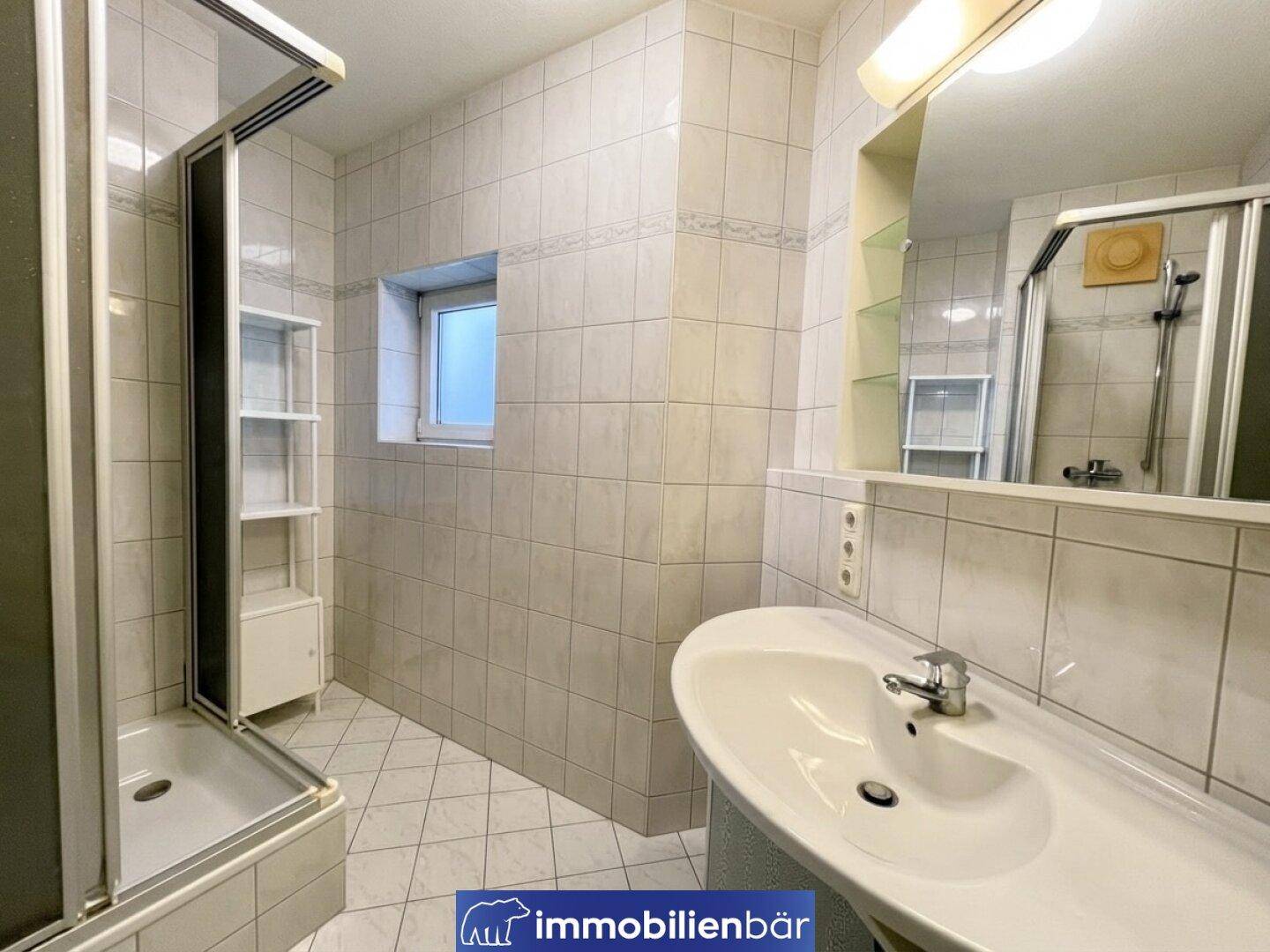 Helles Badezimmer mit Duschkabine, Waschbecken und einem kleinen Fenster für Tageslicht.