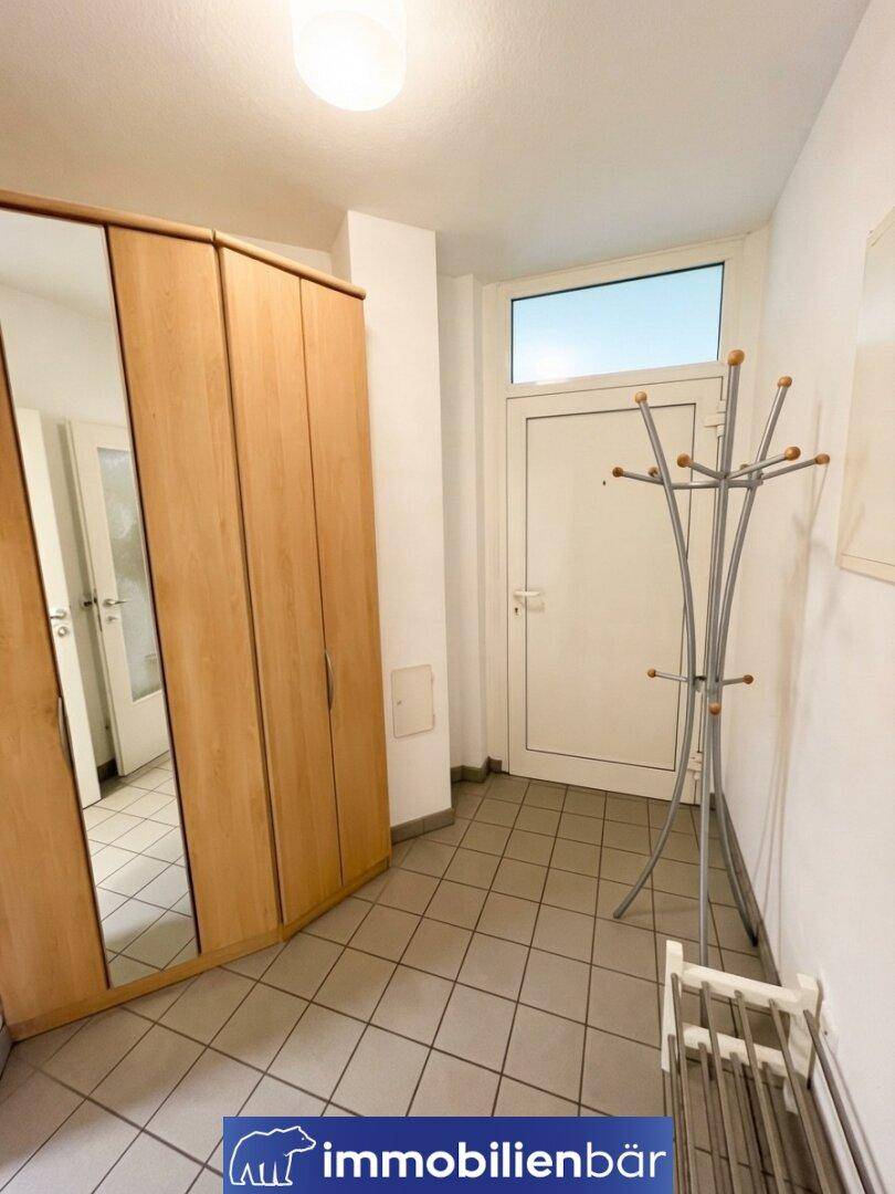 Eingangsbereich mit Fliesenboden, Spiegelschrank und Garderobe, hell durch die Tür mit Fenster.