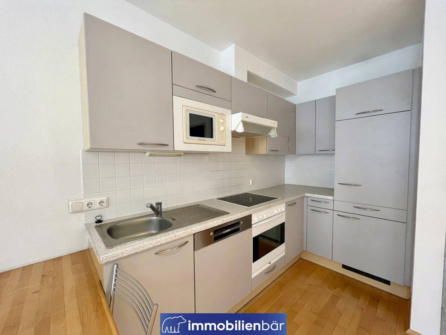 Funktionale Küche mit grauen Schränken, integrierten Geräten und Fliesenrückwand.