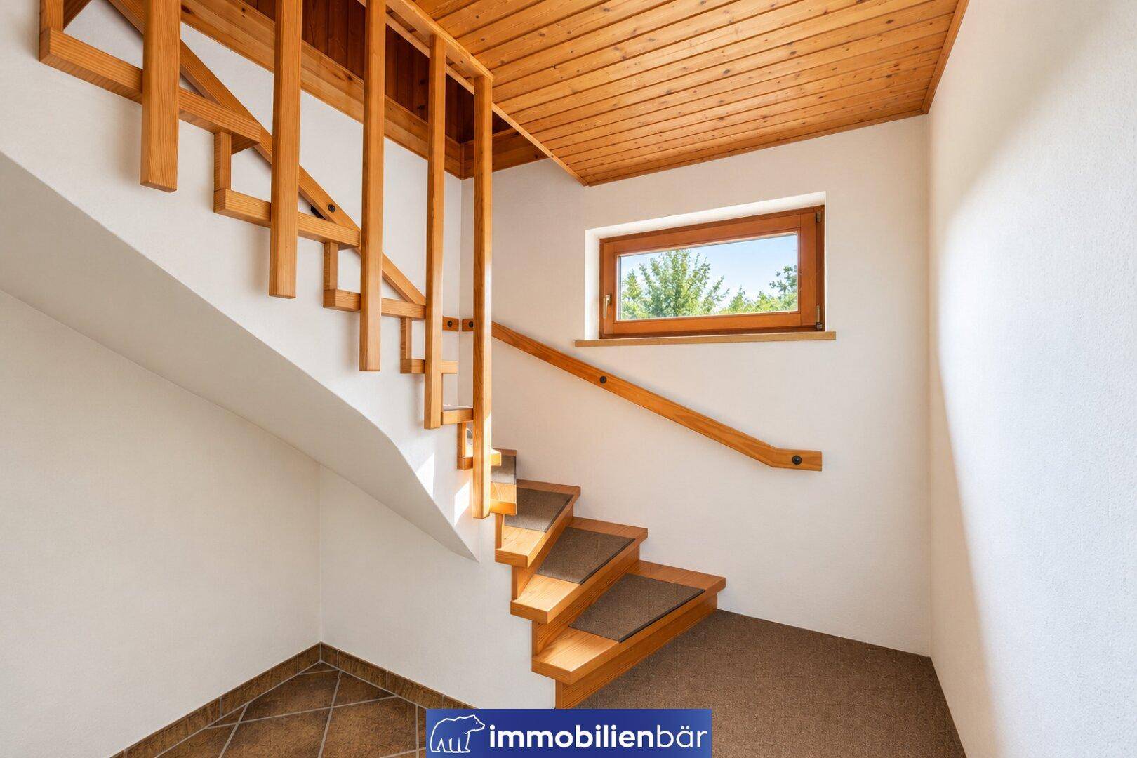 Holztreppe mit Teppichstufen und einem Fenster, das natürliches Licht in den Flur bringt.