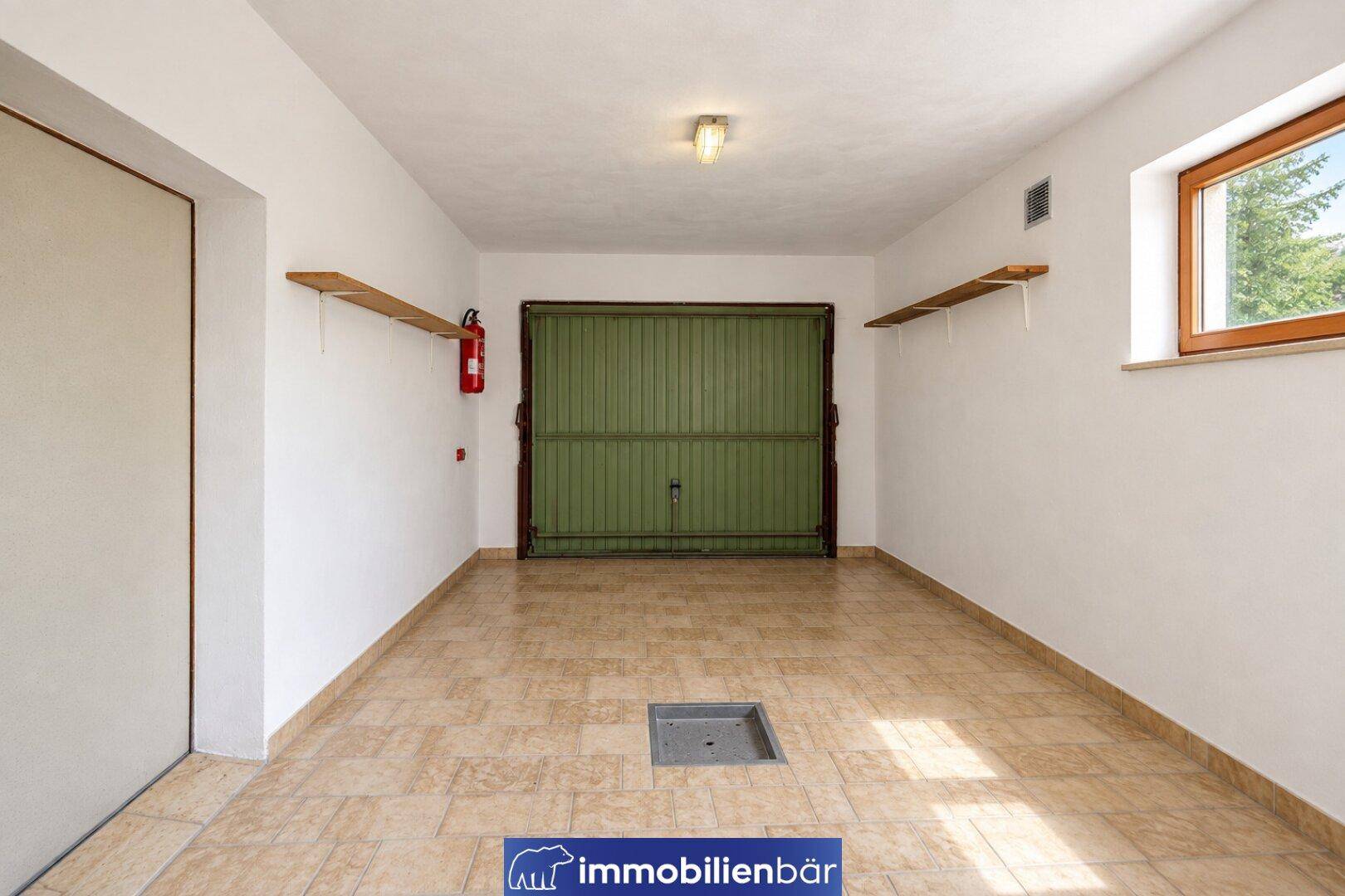 Geräumige Garage mit Fliesenboden, grünem Garagentor und einem kleinen Fenster.