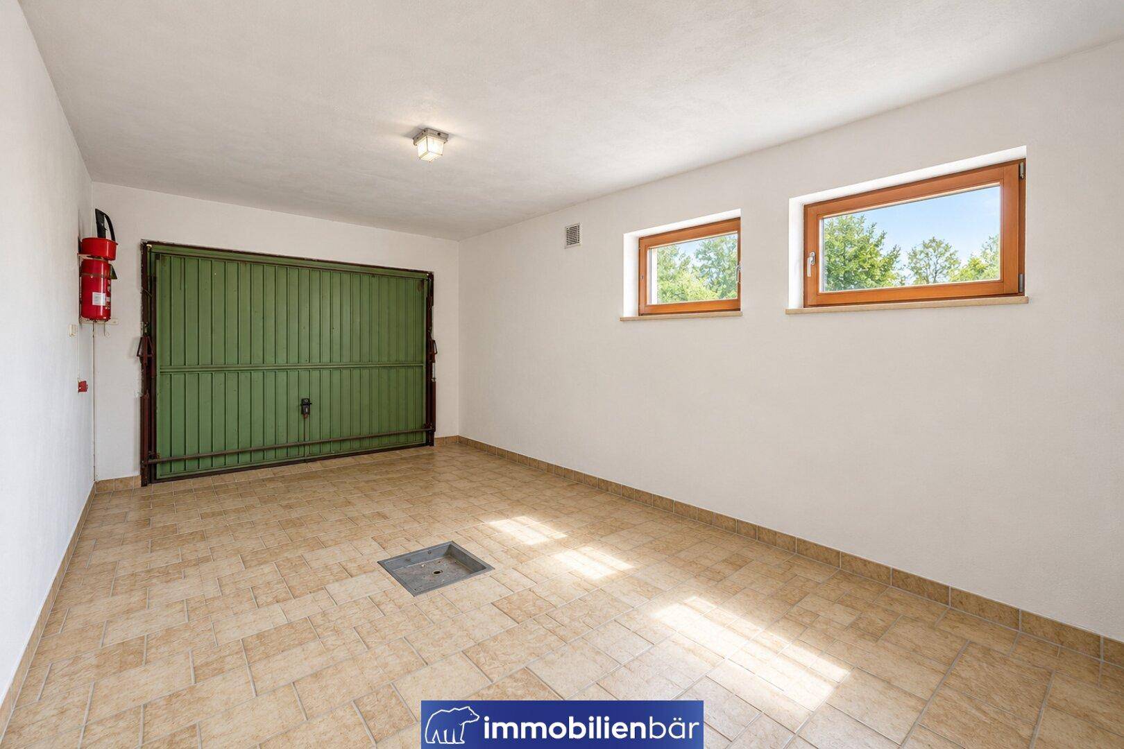 Helle Garage mit Fliesenboden, grünem Tor und zwei Fenstern für Tageslicht.