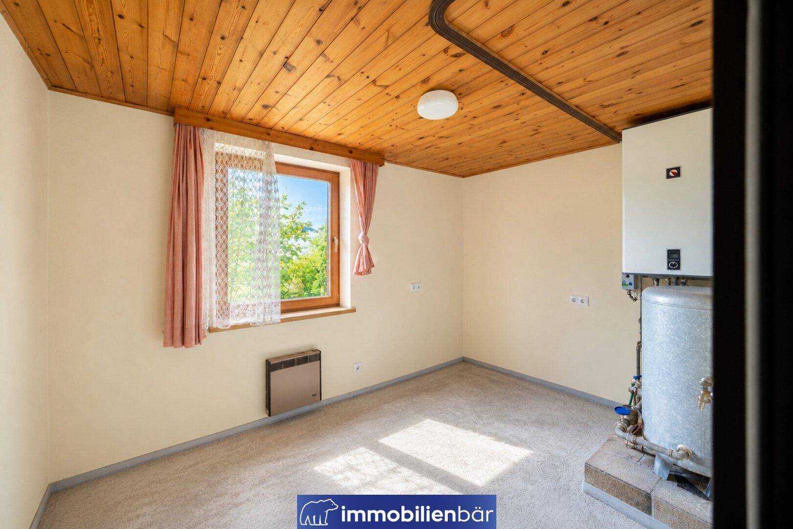 Heller Hauswirtschaftsraum mit Warmwasserbereiter, Boiler und einem Fenster für natürliche Belüftung.