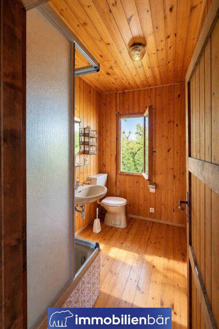 Kleines Badezimmer mit Holzvertäfelung, Toilette, Waschbecken und einem Fenster.