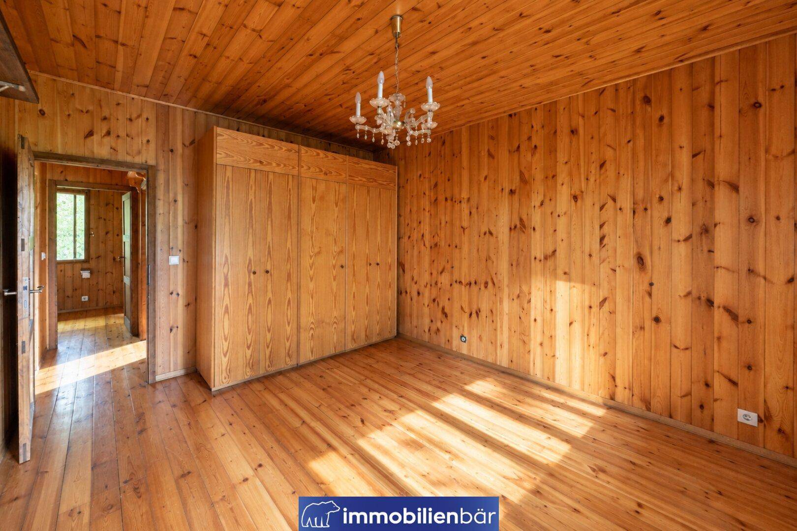Geräumiges Zimmer mit Holzvertäfelung, Holzboden und einem Kronleuchter an der Decke.