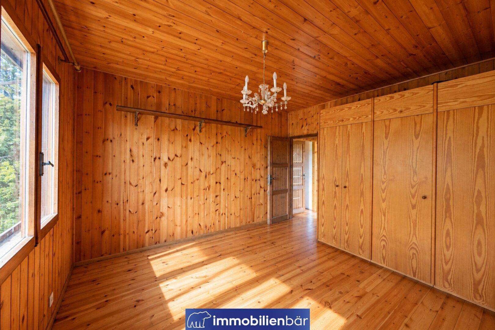 Helles Zimmer mit Holzvertäfelung, Einbauschränken und einem eleganten Kronleuchter.