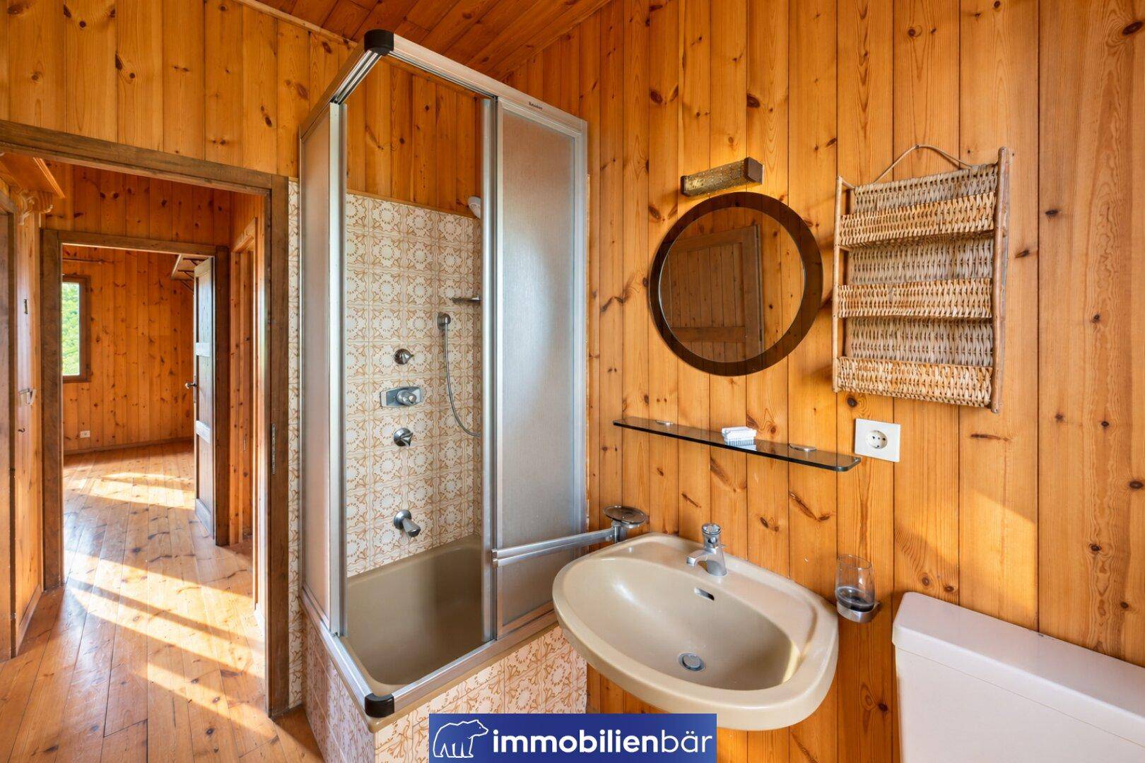 Rustikales Badezimmer mit Holzvertäfelung, Duschkabine und älterem Waschbecken.