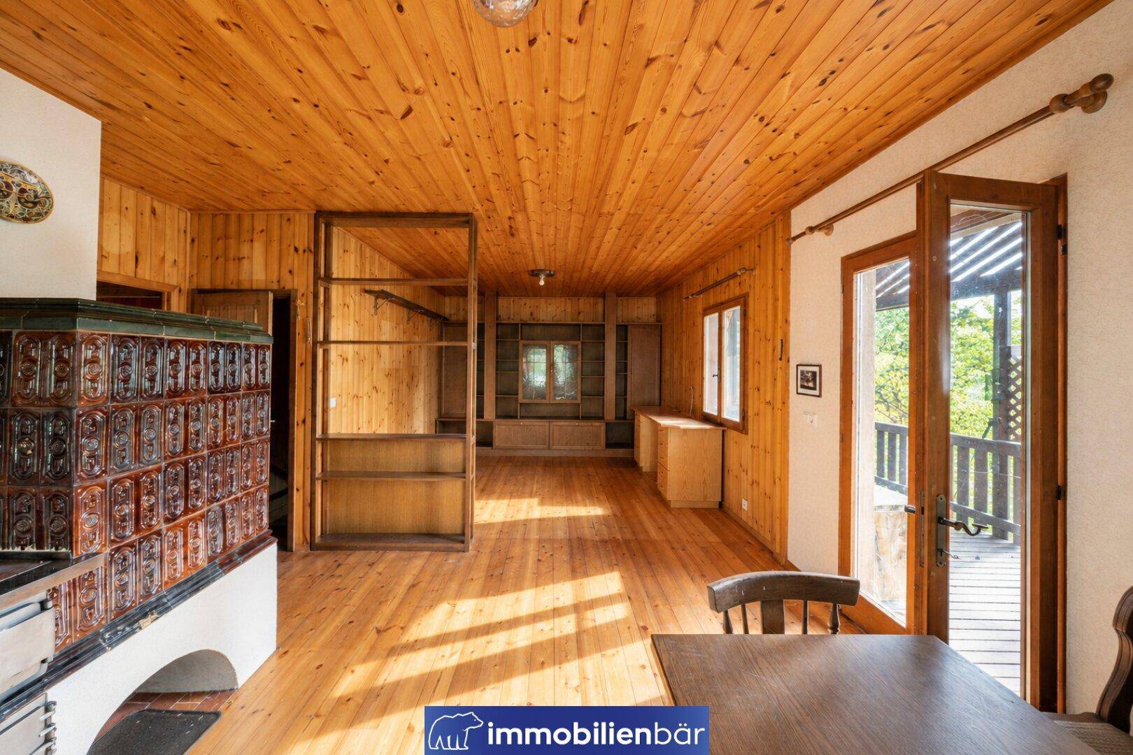 Geräumiger Wohn-Essbereich mit Kachelofen, Holzboden und Zugang zum Balkon.