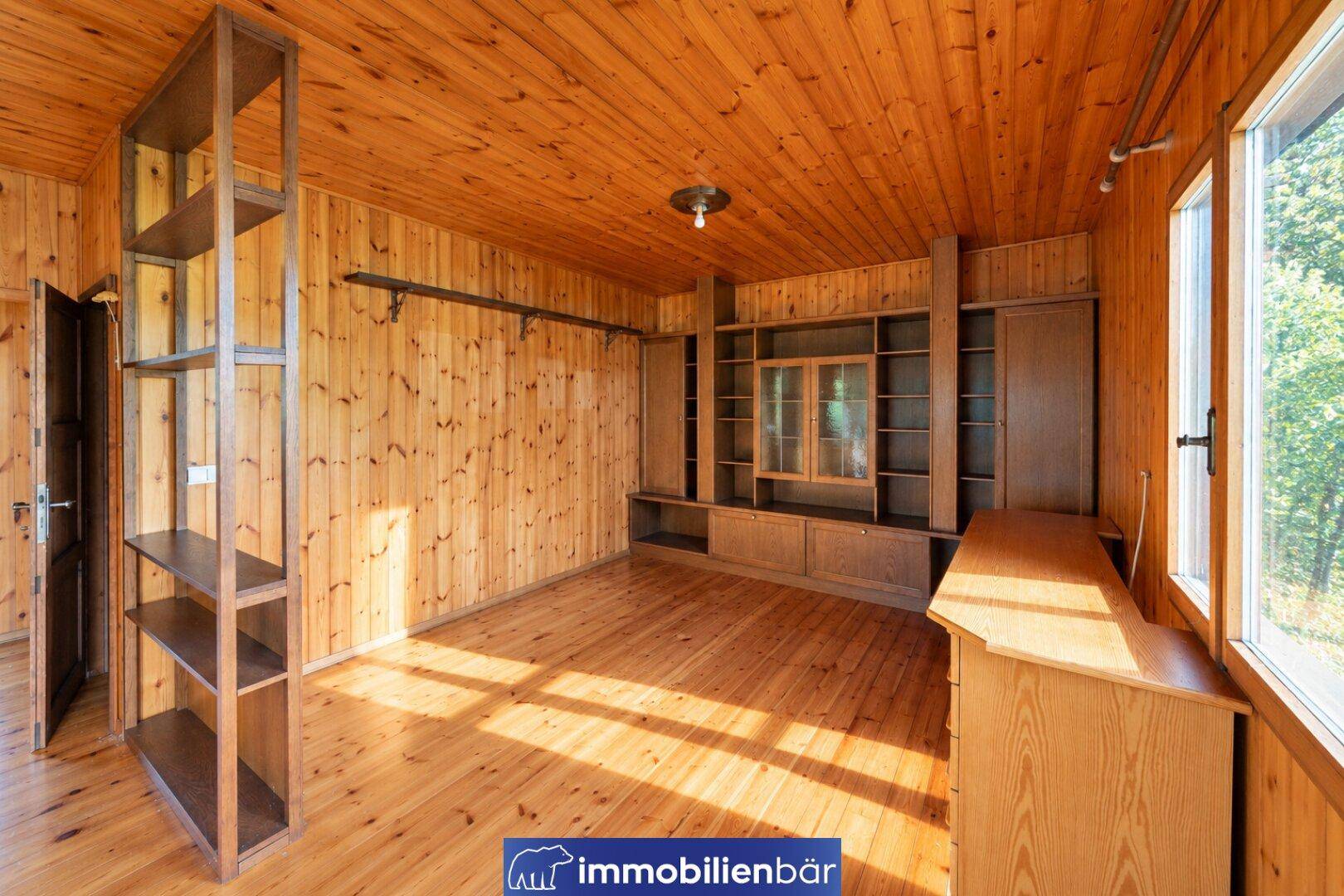 Wohnzimmer mit Holzvertäfelung, Einbauschränken und Blick ins Grüne durch das große Fenster.