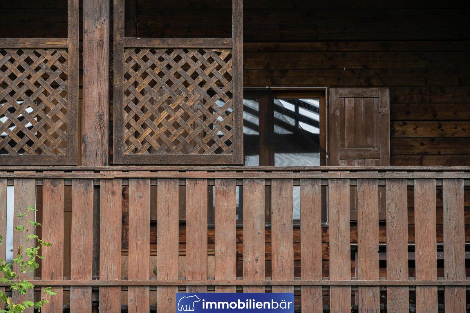 Detailansicht eines Holzgeländers und der Fassade eines traditionellen Holzhauses.