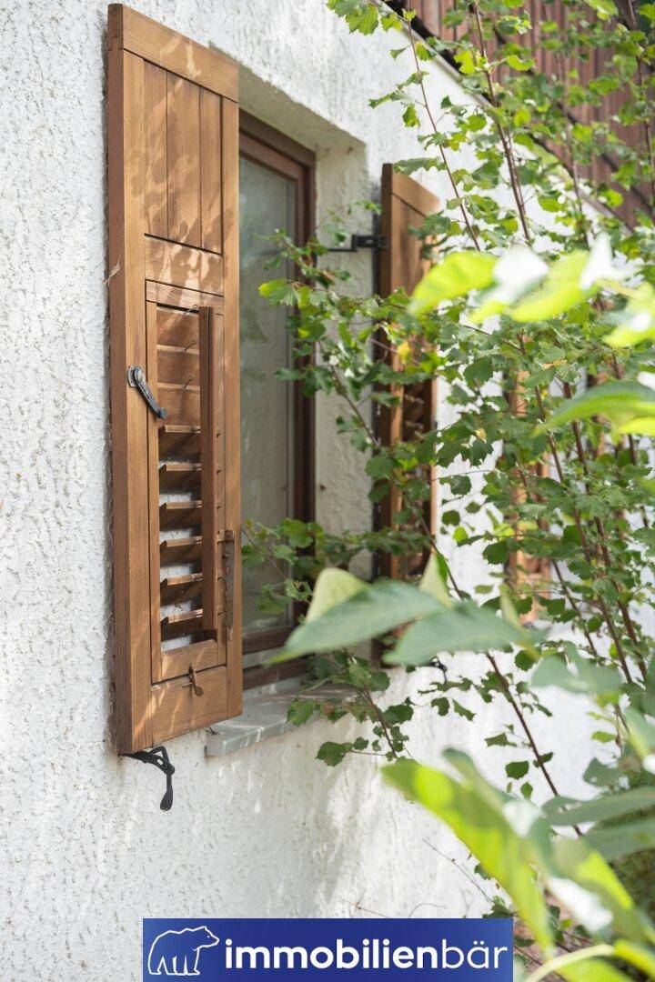 Seitliche Ansicht eines Fensters mit geöffneten Holzläden an einer strukturierten Fassade.