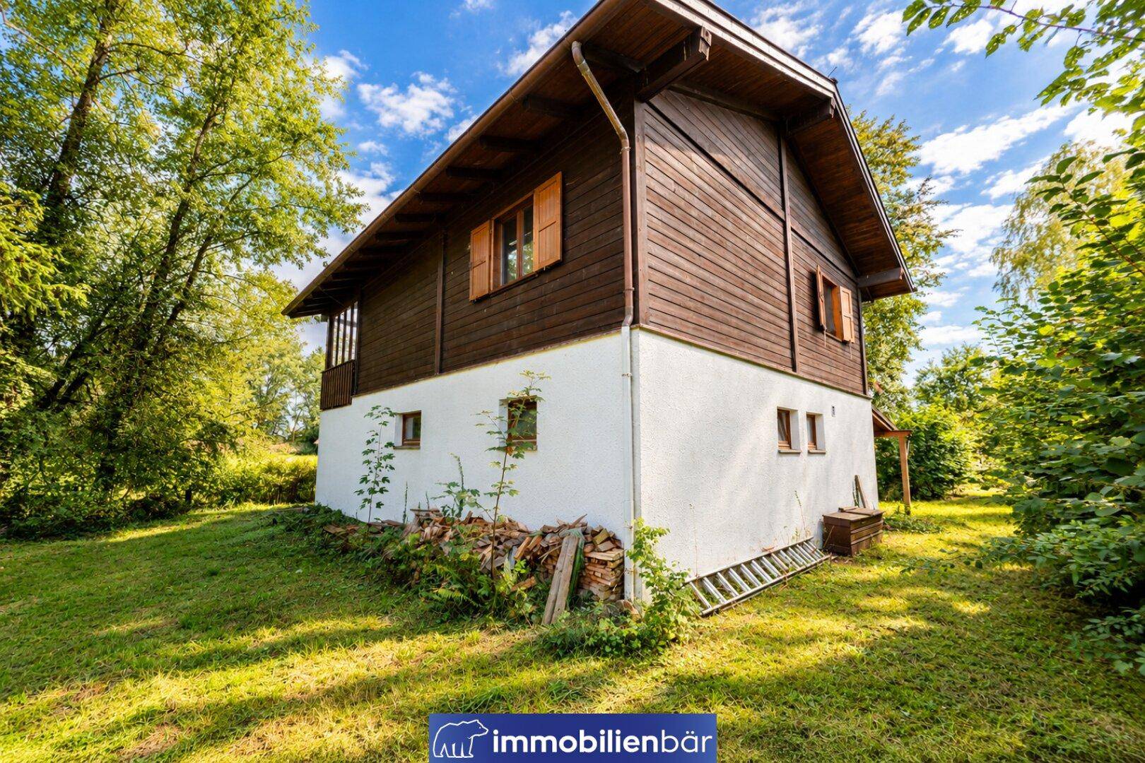 Freistehendes Holzhaus mit weißem Sockel und Satteldach, umgeben von einem großen Garten.