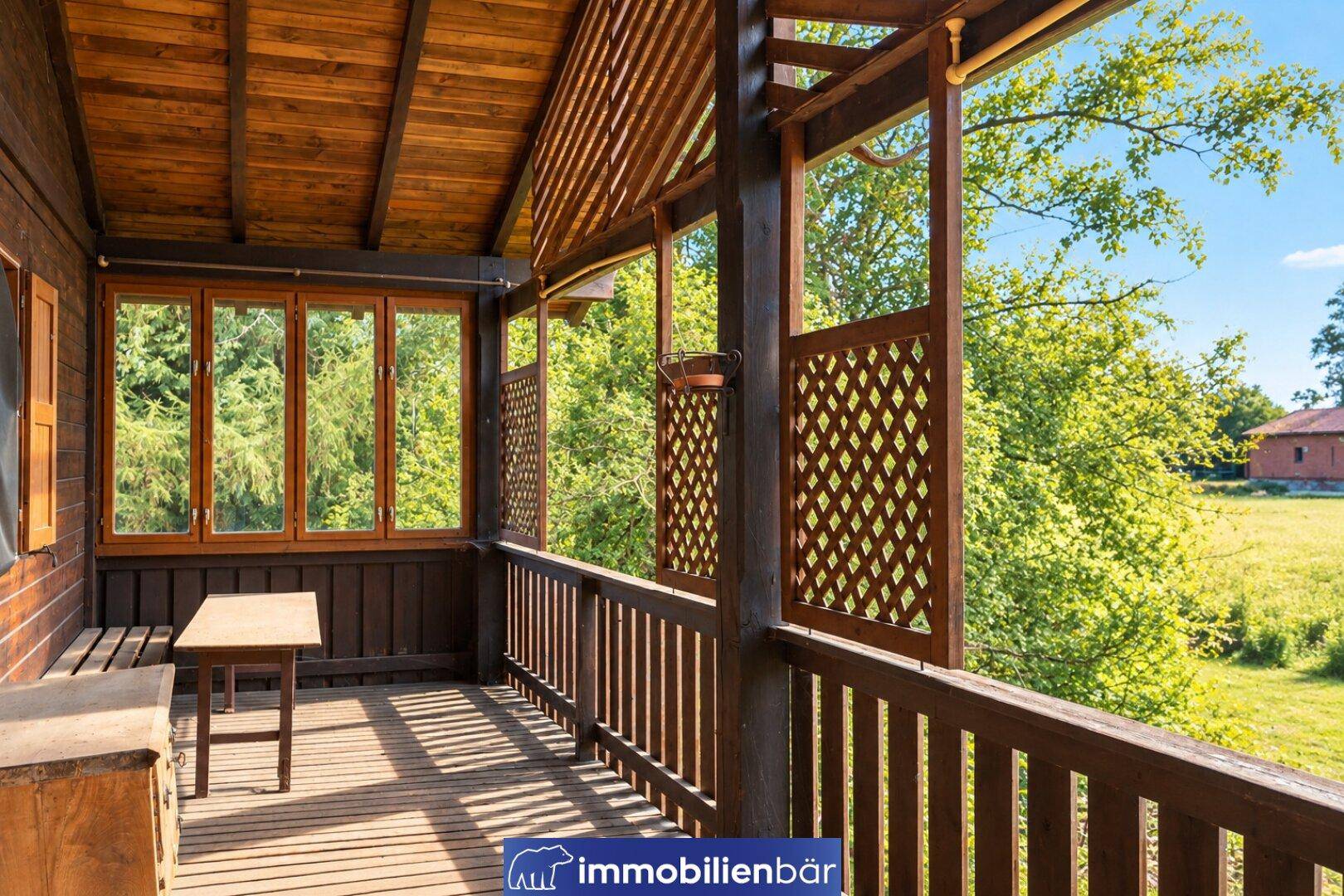 Überdachter Holzbalkon mit Sitzgelegenheiten und weitem Blick auf die grüne Landschaft.