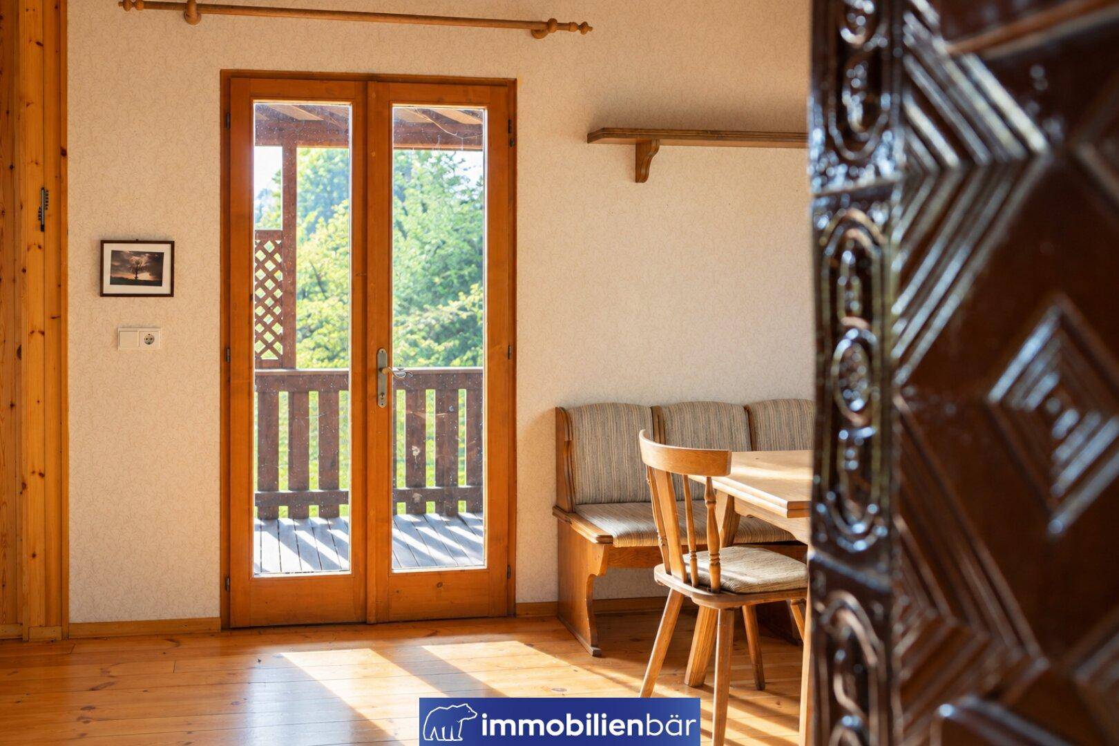 Essbereich mit Holztisch, Sitzbank und Zugang zu einem sonnigen Balkon.