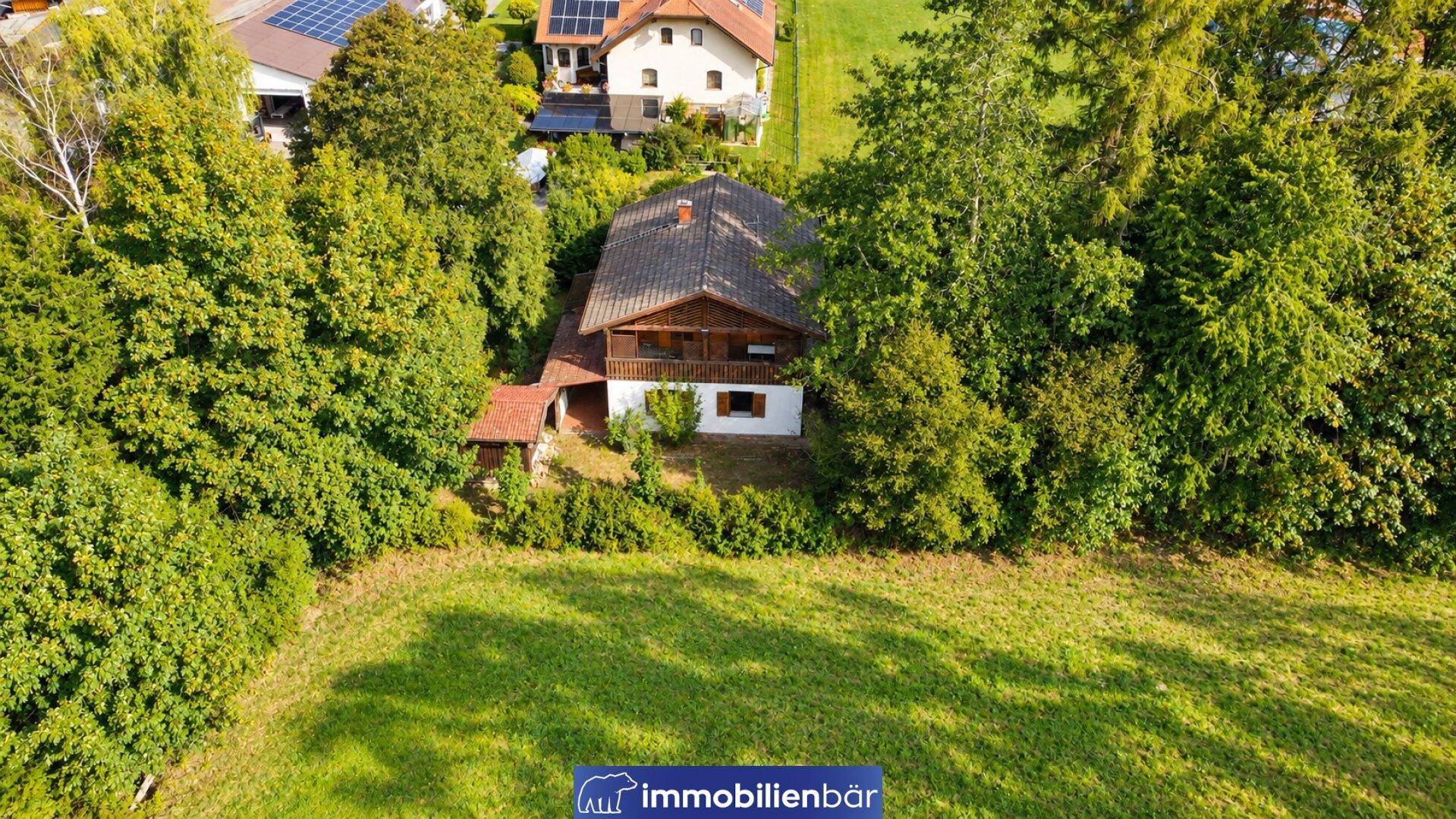 Luftaufnahme eines freistehenden Holzhauses umgeben von Bäumen und einer großen Wiese.