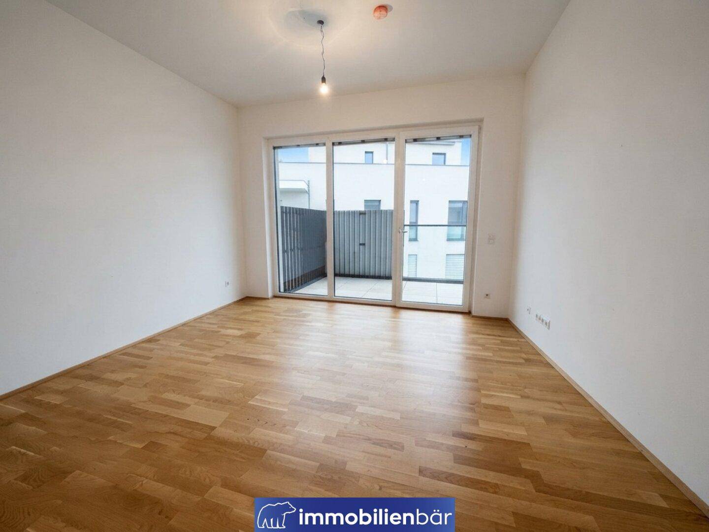 Geräumiges, unmöbliertes Zimmer mit Holzboden und großer Schiebetür zum Außenbereich.