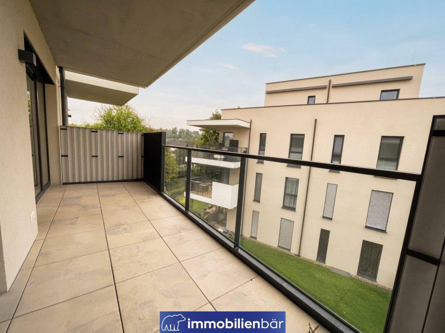 Geräumiger Balkon mit Fliesenboden und Glasgeländer, bietet einen weiten Blick auf die Umgebung.