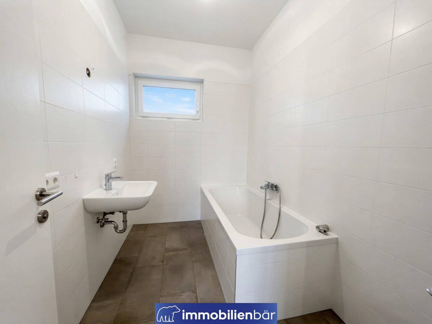 Helles Badezimmer mit Badewanne, Waschbecken und Fenster, komplett gefliest.