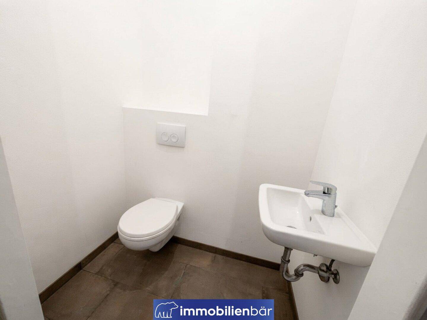Separates WC mit wandhängender Toilette und kleinem Waschbecken, modern gefliest.