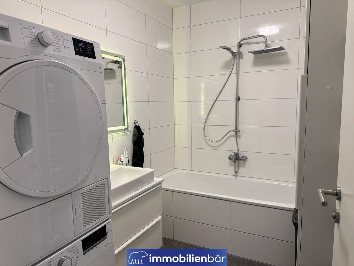Modernes Badezimmer mit weißen Fliesen, Badewanne, Waschbecken und Waschtrockner.