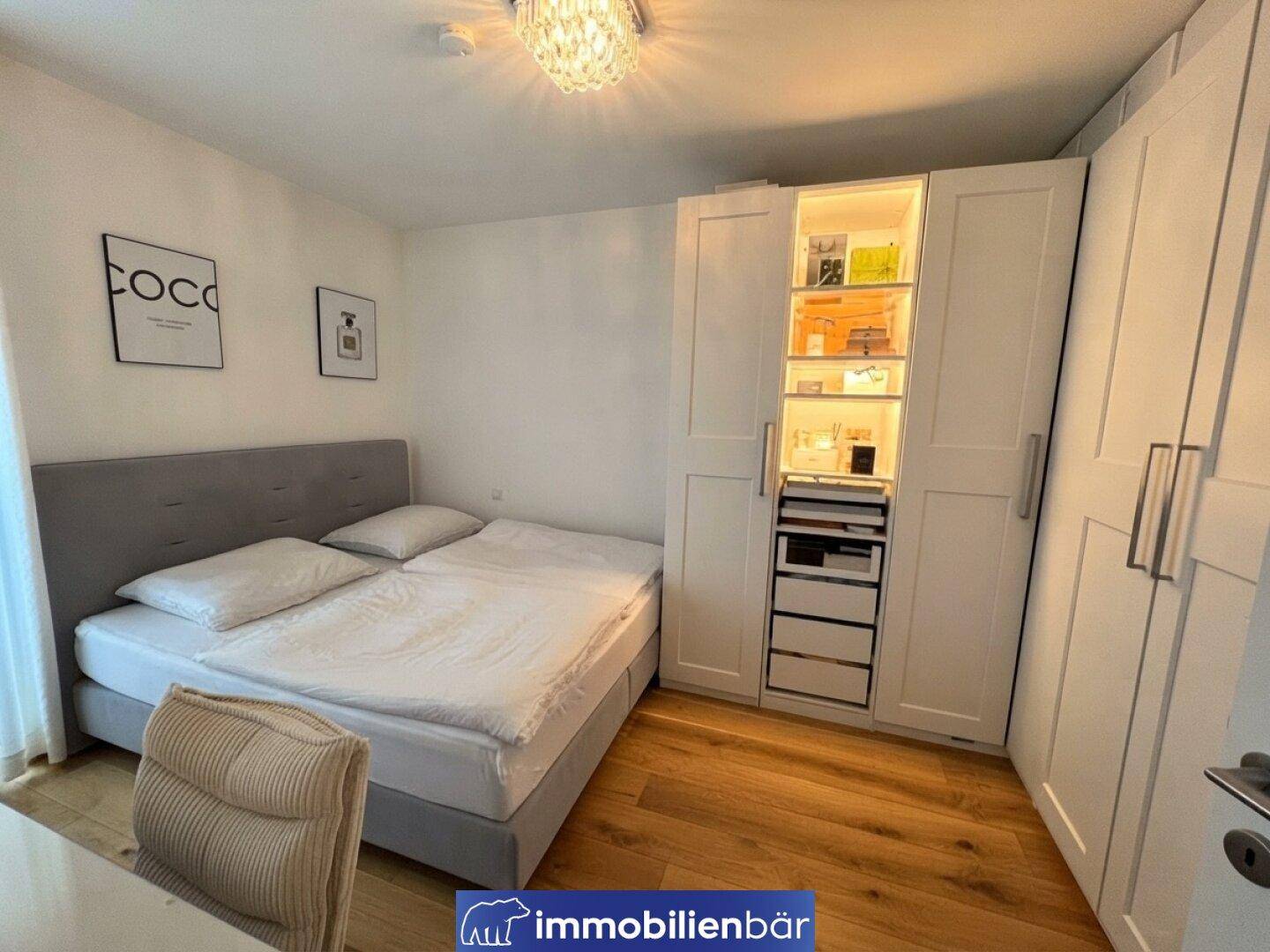 Schlafzimmer mit Doppelbett und praktischen weißen Einbauschränken mit Beleuchtung.