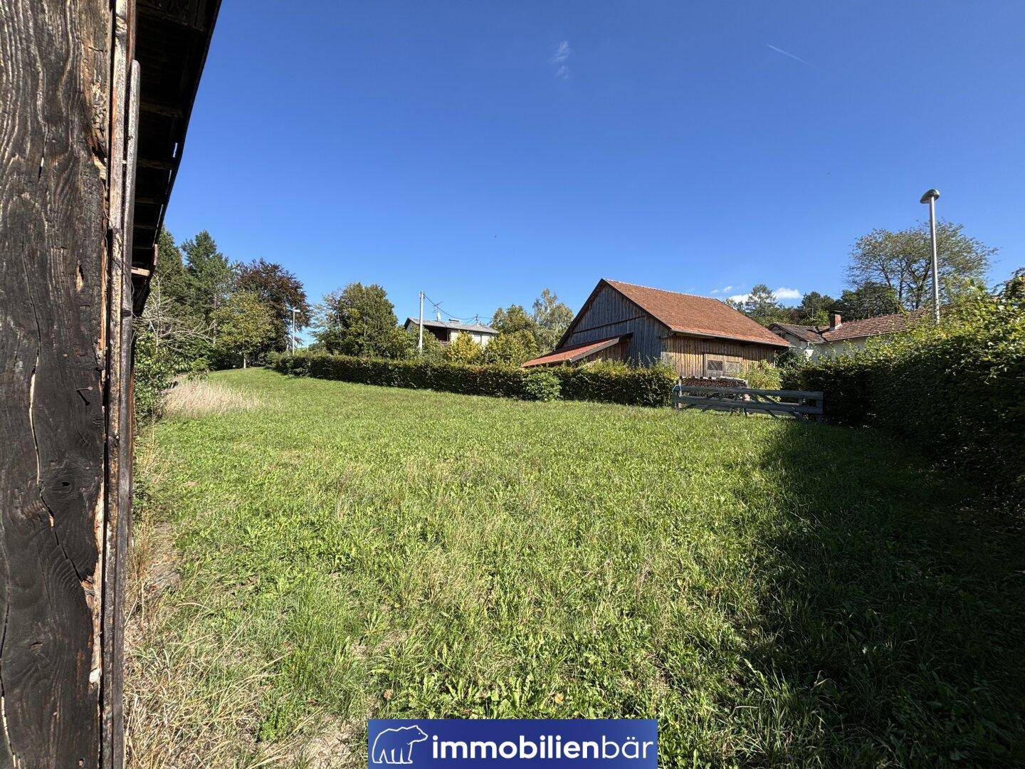 Weitläufige Grünfläche mit Blick auf weitere Gebäude und eine Hecke im Hintergrund unter blauem Himmel.