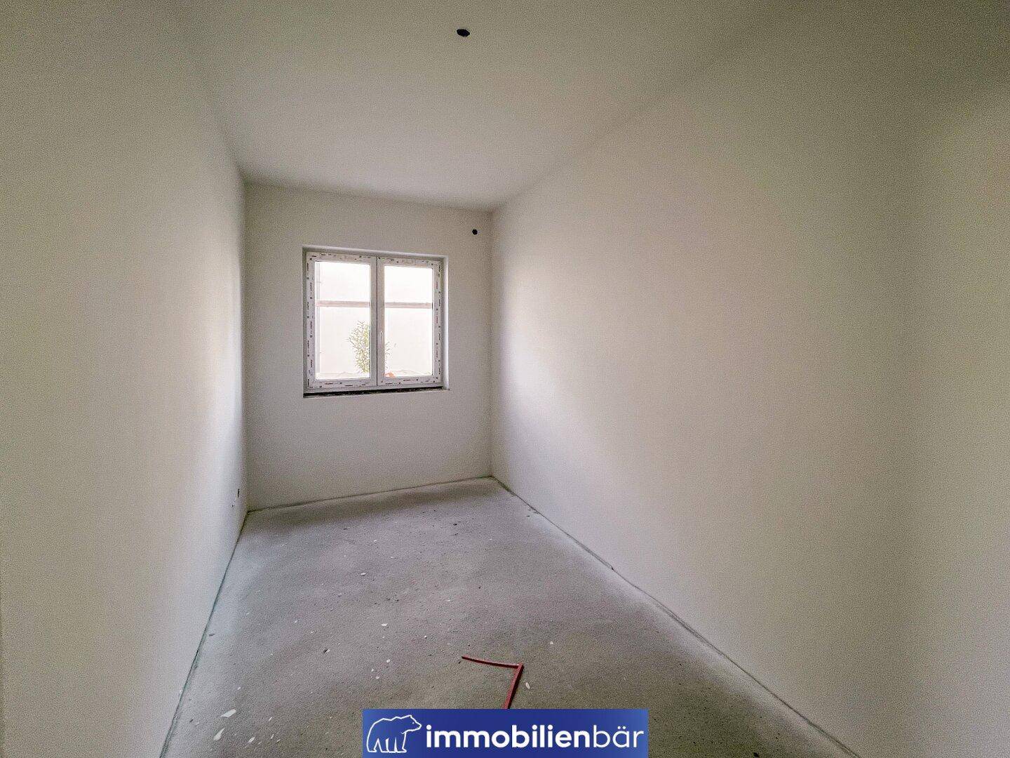 Kleiner, unfertiger Raum mit einem Fenster und Betonboden, bereit für den Innenausbau.