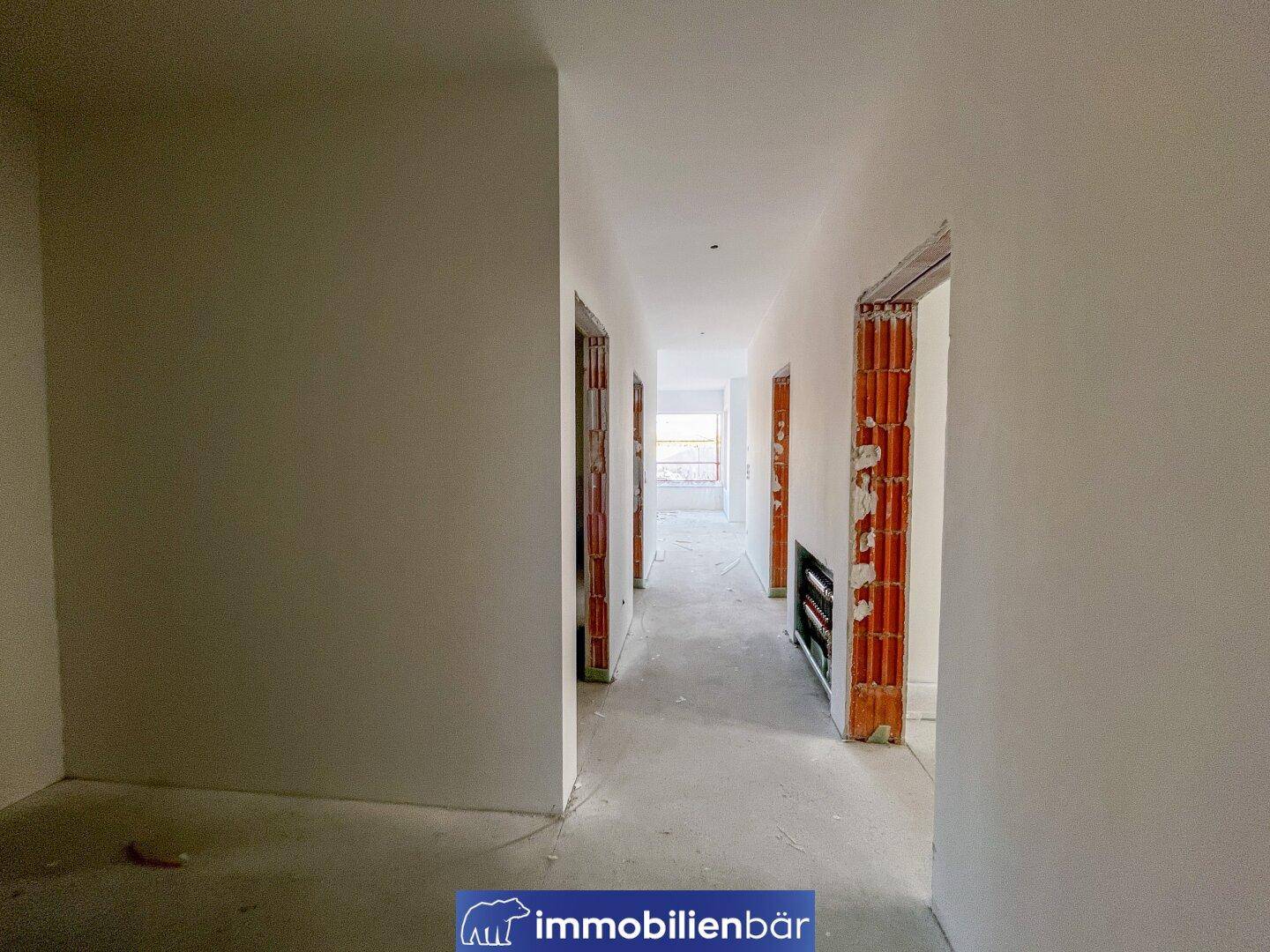 Langer, unfertiger Flur mit Rohbau-Türrahmen und Betonboden, bereit für den Ausbau.