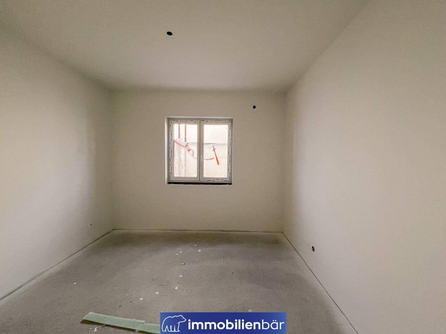 Heller, unfertiger Raum mit einem Fenster und Betonboden, bereit für die individuelle Gestaltung.