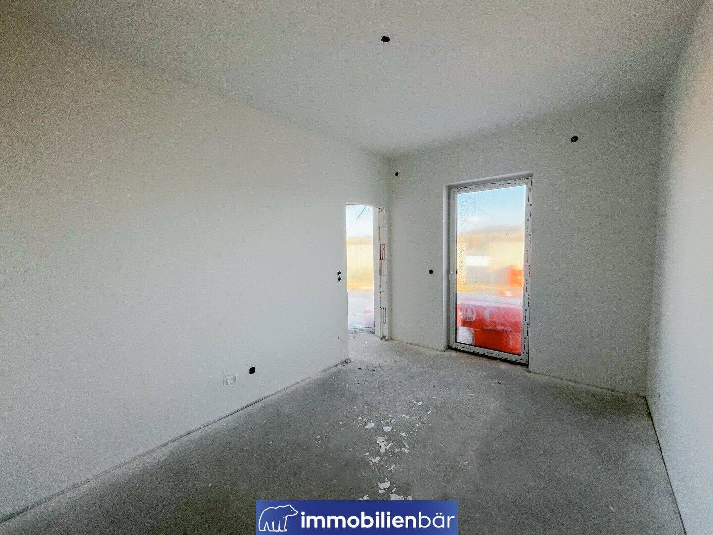 Heller Rohbau-Raum mit Fenster und Türöffnung, bereit für den Innenausbau.
