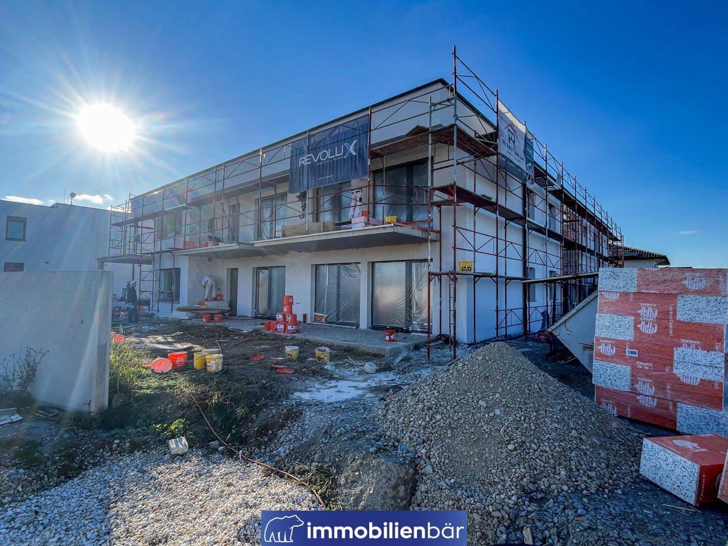 Baustelle eines modernen Wohngebäudes mit Gerüst und Sonnenschein.